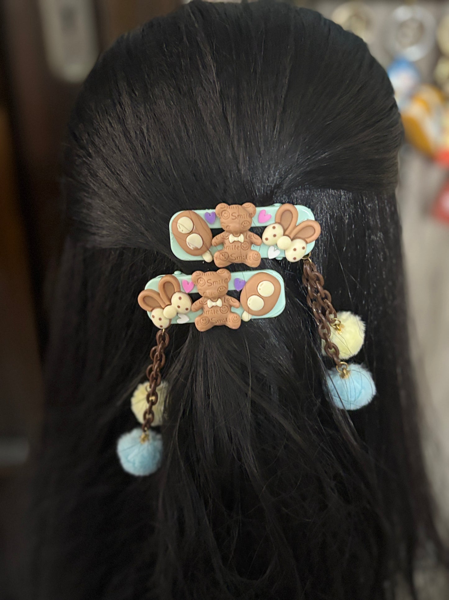 Cute kids’ hair clips with chocolate teddy bear, bunny ears, and soft Pom Pom dangles in blue and yellow—adorable and fun accessory for stylish hairstyles.