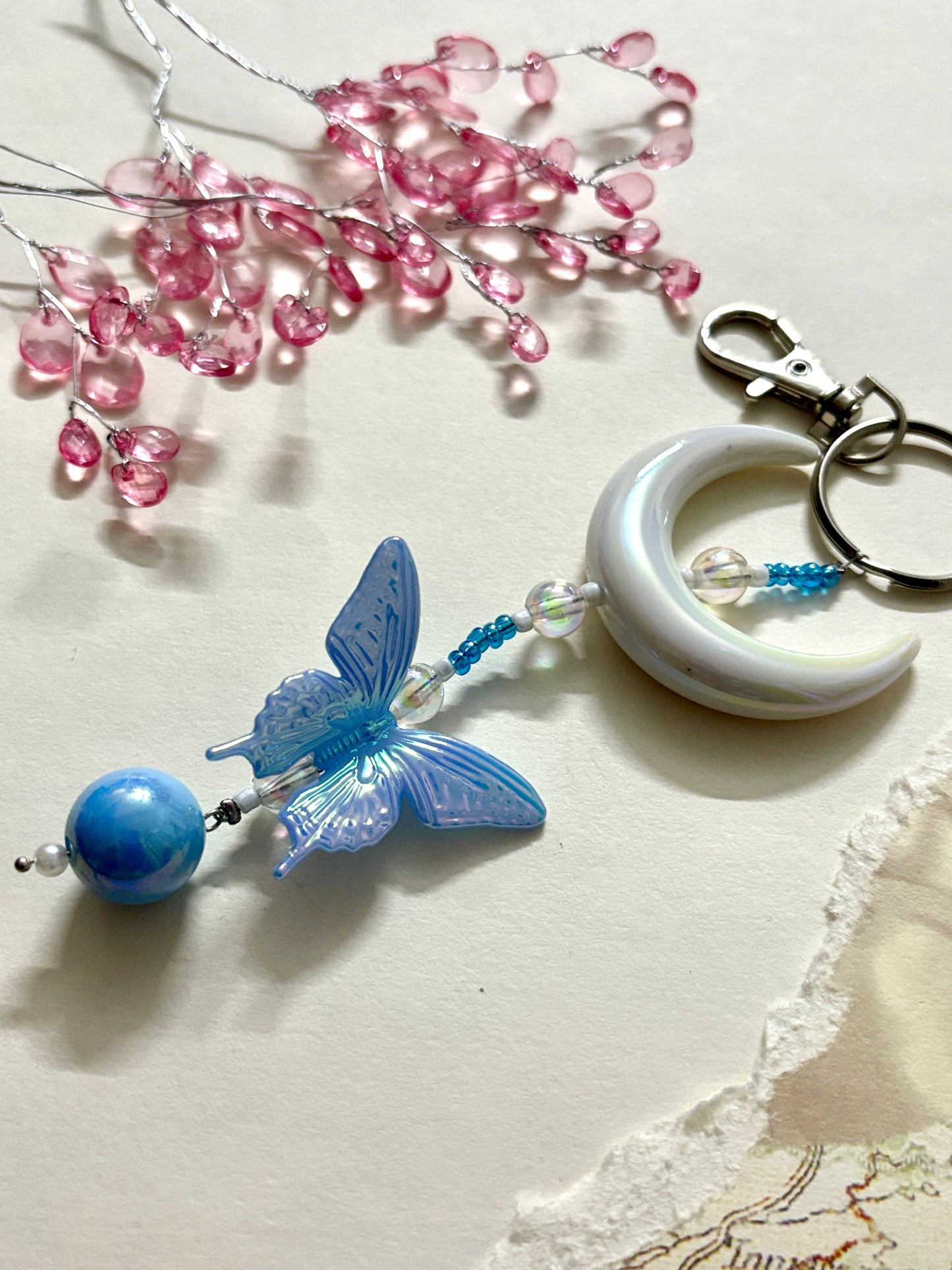 Elegant bag charm with moon, butterfly, and bead details hanging from a black leather handbag. Adds a whimsical and stylish touch to any bag.