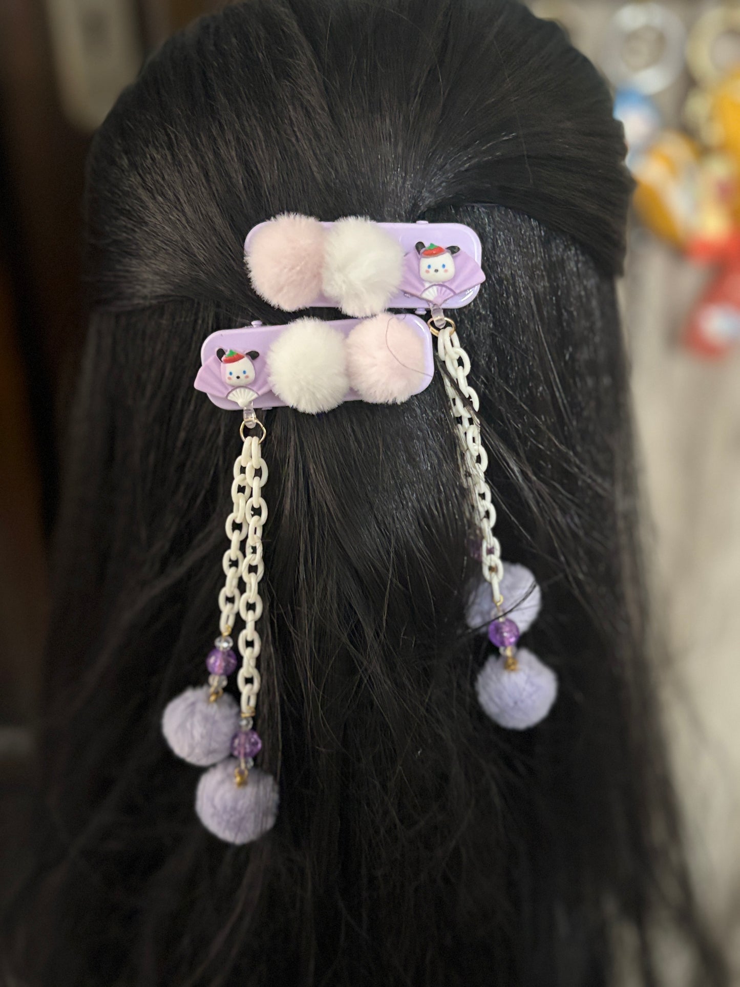 Cute purple Pom Pom hair clips with white chains, beads & soft fluff balls—adorable kids’ hair accessory shown on display and styled on dark hair.
