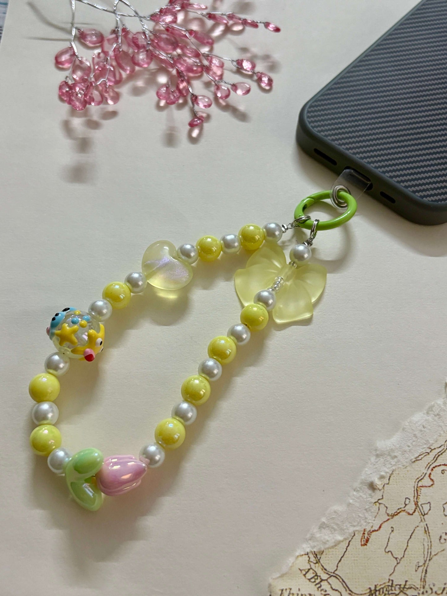 A beaded phone charm strap featuring glossy pearl-like beads, miniature character and flower charms, and a loop attachment; designed as a cute and functional phone accessory for personalization and added grip.