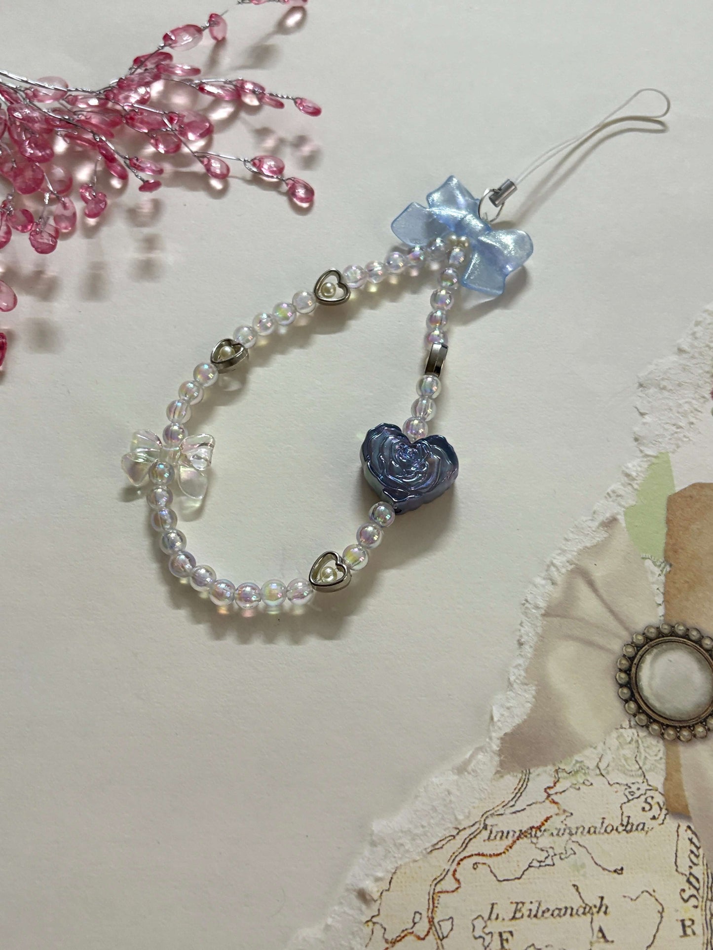 Beaded phone charm featuring a rose-shaped heart, delicate bow, and small heart accents; designed for attaching to mobile phones, adding a stylish and cute touch.