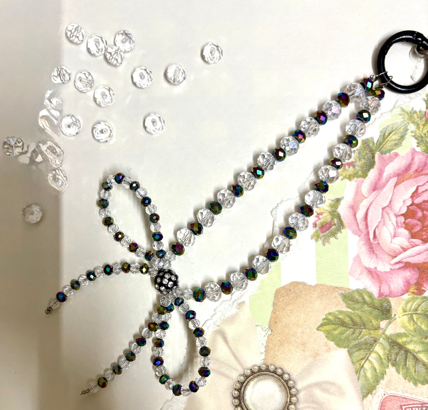 Elegant beaded phone charm featuring a delicate crystal bow design with faceted beads and a rhinestone center, styled with vintage floral paper.