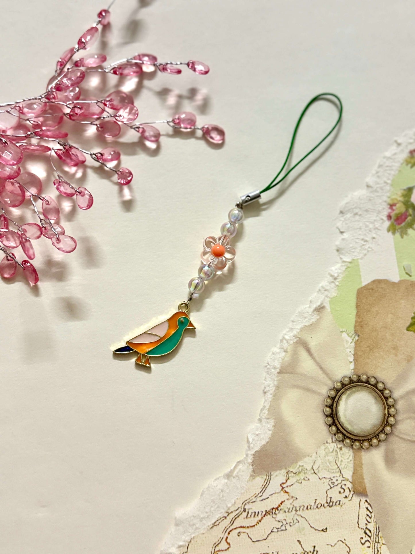 Minimalist phone charm featuring a colorful bird pendant and a floral bead accent on a beaded strap, attached with a loop for easy phone connection.