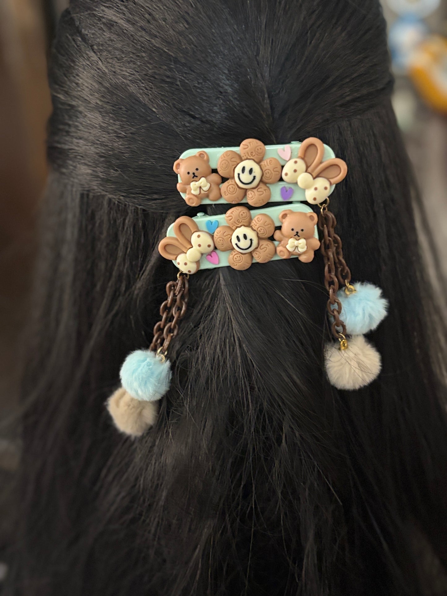 Cute chocolate-themed hair clips with smiling flowers, teddy bears, and bunnies. Dangling pastel pom-poms add a playful flair to your look.