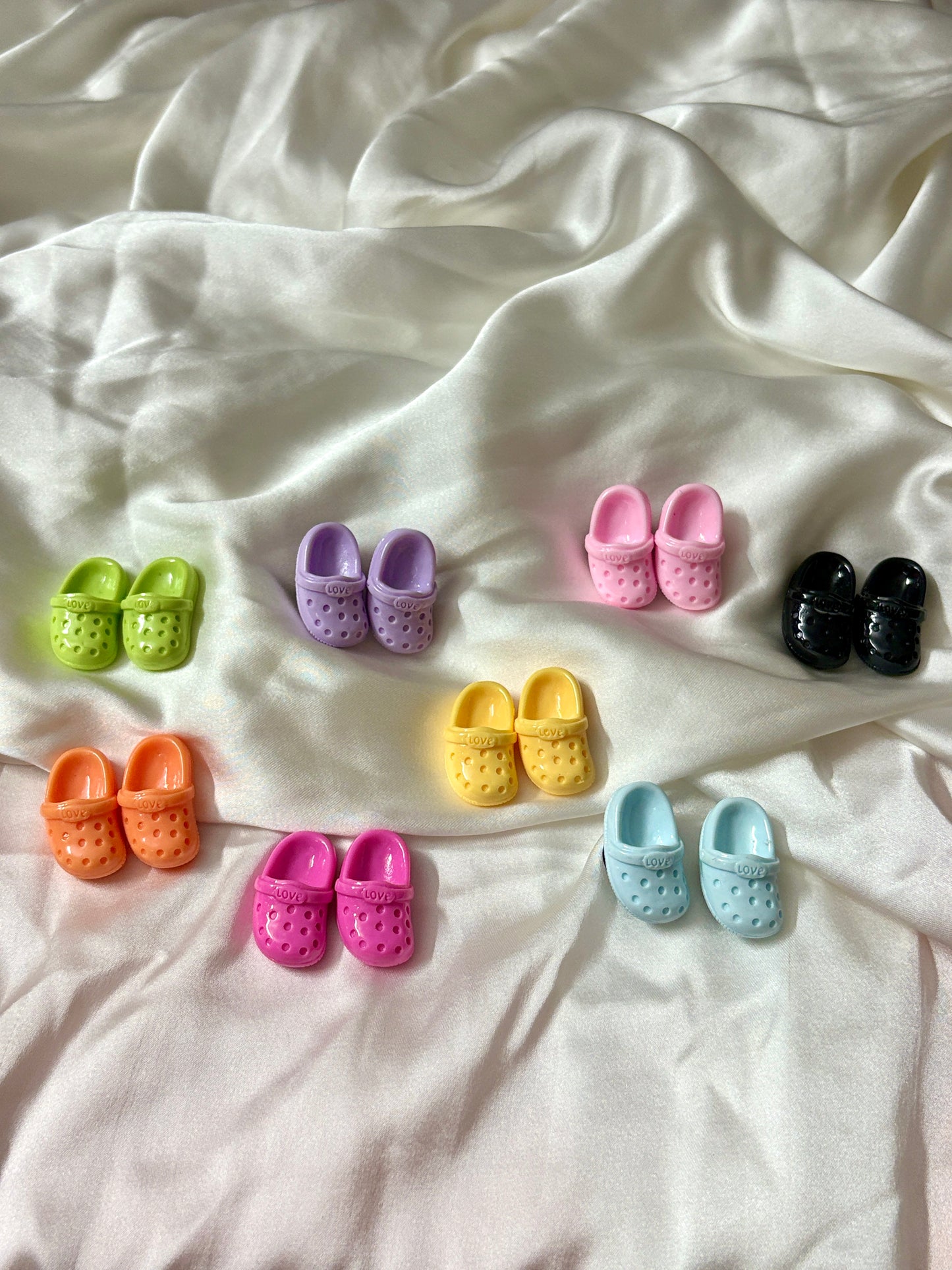 Colorful Crocs-shaped Jibbitz charms in matching pairs, with vibrant shades like pink, blue, yellow, black, and more—perfect for a quirky Crocs upgrade.