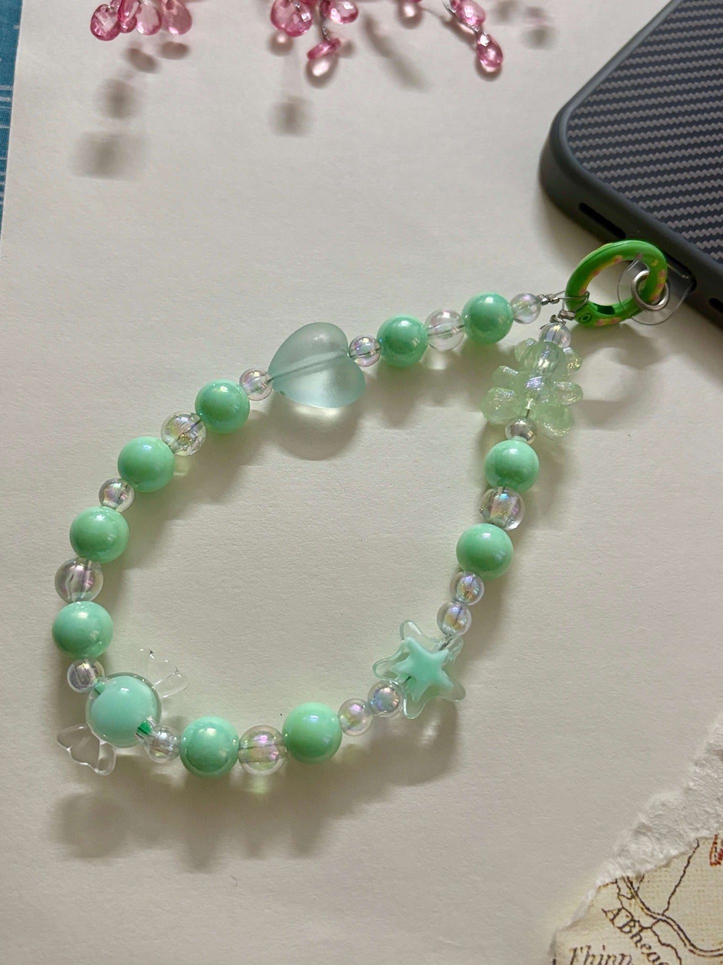 Beaded phone charm with heart, star, and teddy bear accents, designed to hang from a mobile device; features pearl and translucent beads for a cute and playful look.