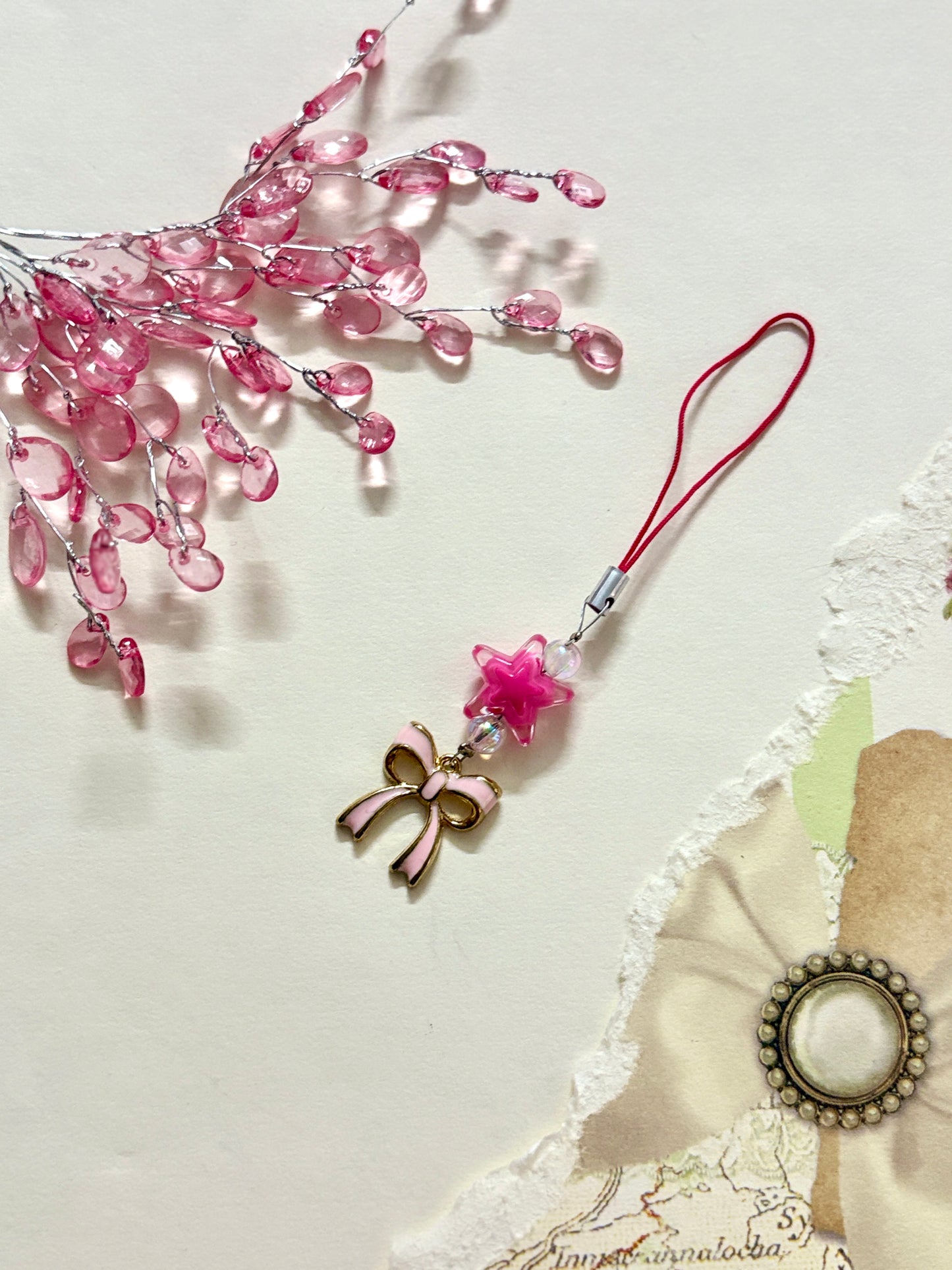 Cute phone charm featuring a star bead, enamel bow charm, and iridescent beads, styled with soft floral decor and a delicate strap.