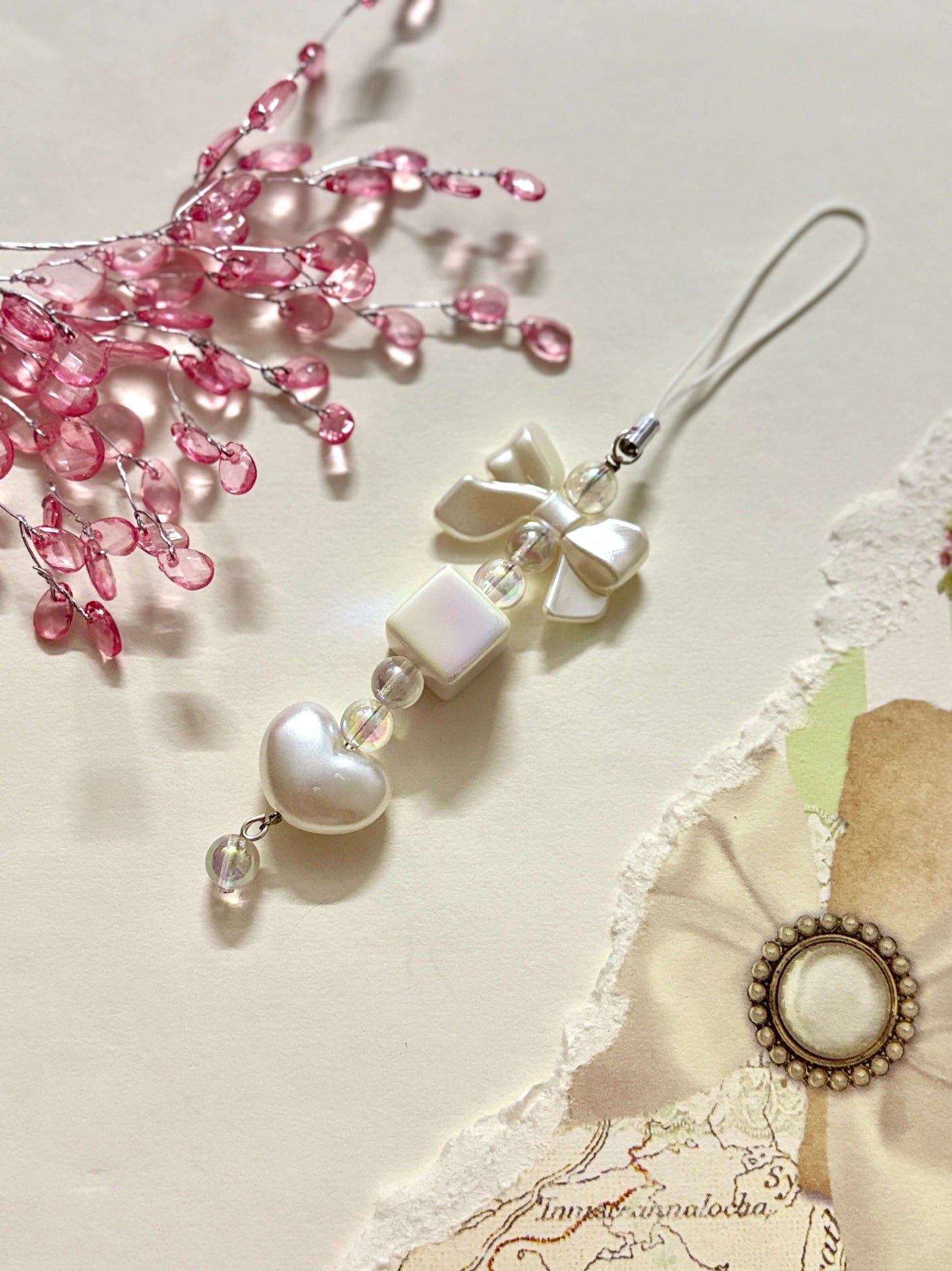 Minimalist phone charm featuring a glossy heart, cube, and bow beads with a clear loop strap, designed for decorating phones, bags, or keychains.