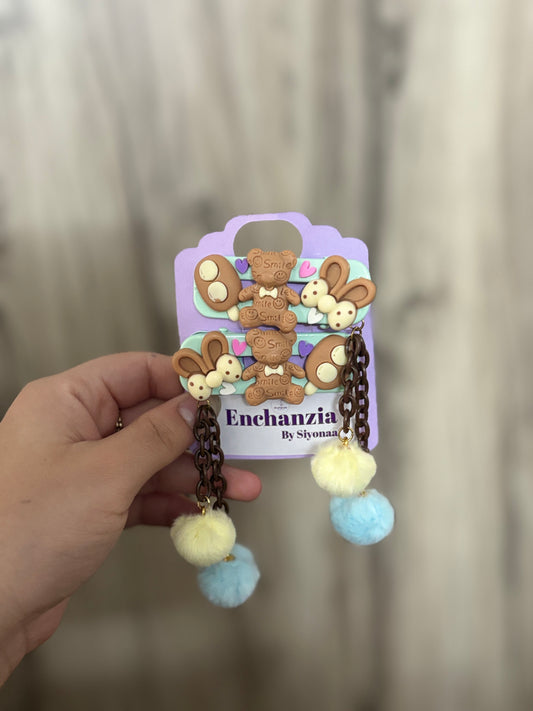 Cute kids’ hair clips with chocolate teddy bear, bunny ears, and soft Pom Pom dangles in blue and yellow—adorable and fun accessory for stylish hairstyles.