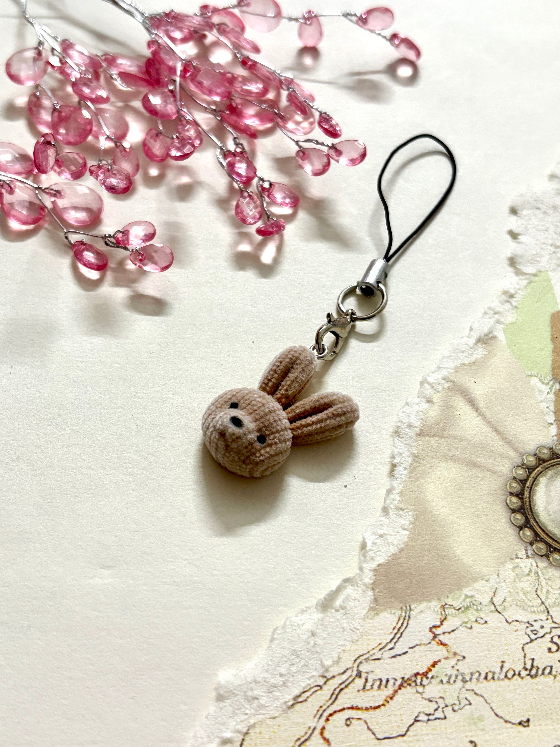 Soft brown plush bunny phone charm with black strap, cute face, and velvet texture. Aesthetic animal accessory for phone, bag, or keyring use.
