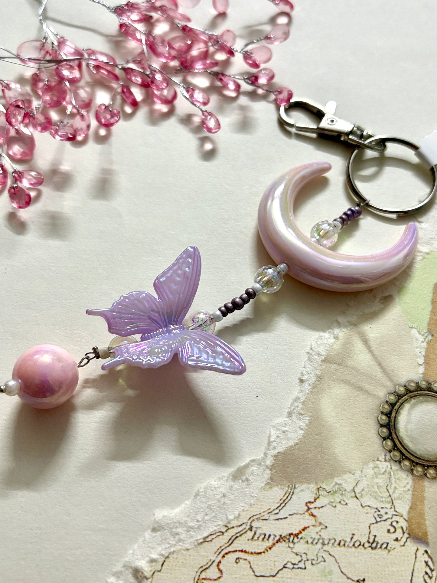 Elegant bag charm with moon, butterfly, and bead details hanging from a black leather handbag. Adds a whimsical and stylish touch to any bag.