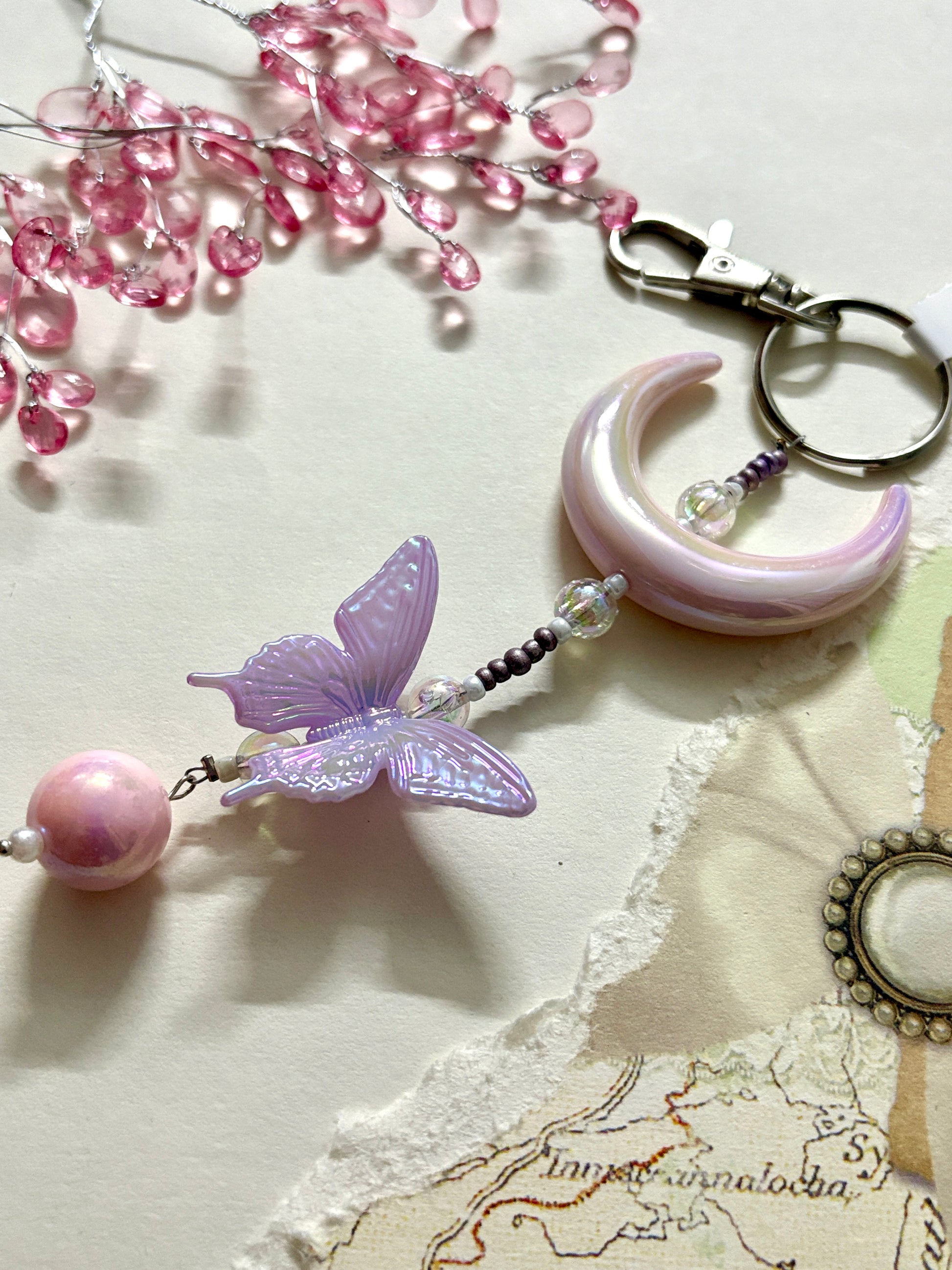 Elegant bag charm with moon, butterfly, and bead details hanging from a black leather handbag. Adds a whimsical and stylish touch to any bag.