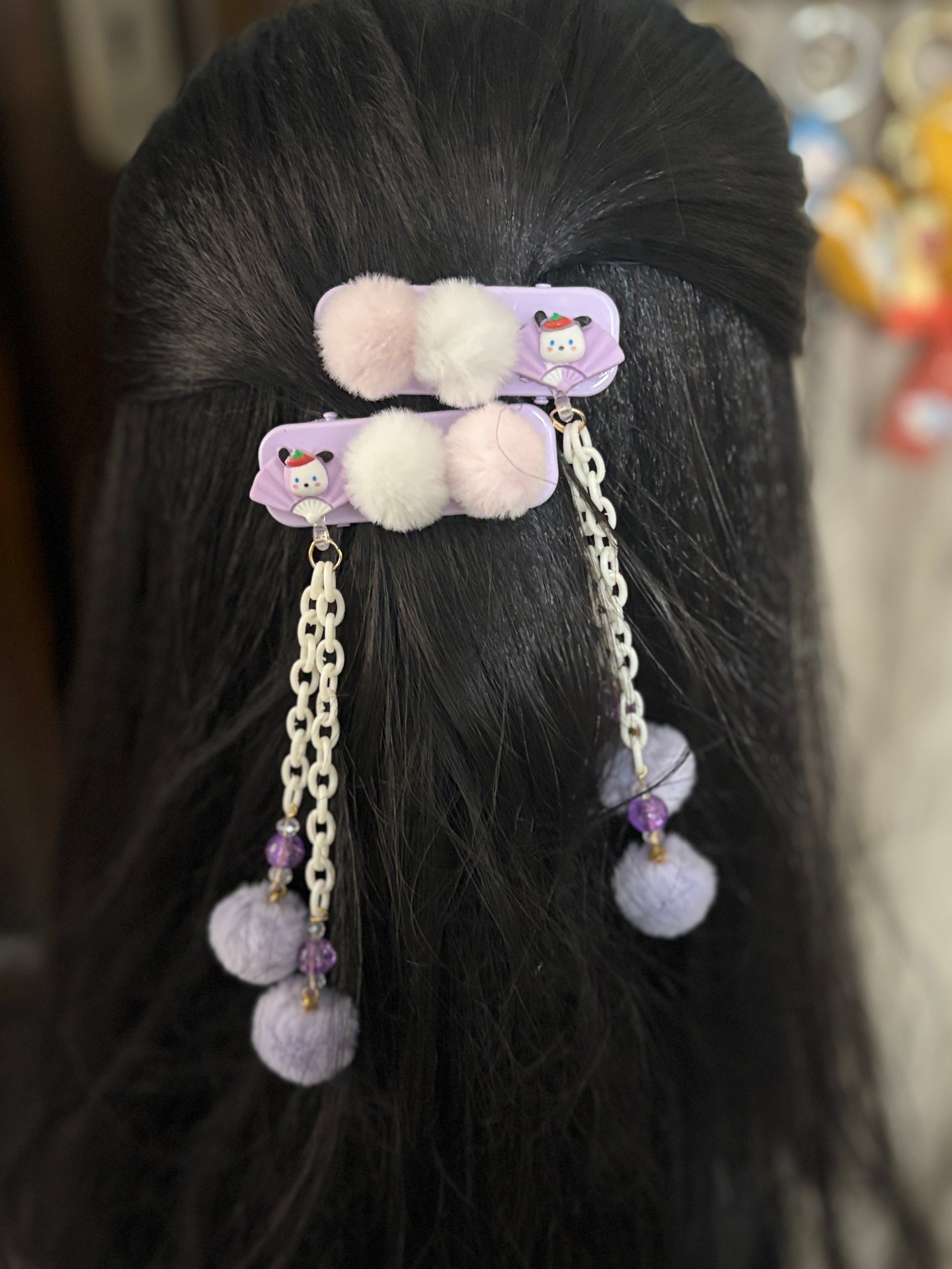 Cute purple Pom Pom hair clips with white chains, beads & soft fluff balls—adorable kids’ hair accessory shown on display and styled on dark hair.
