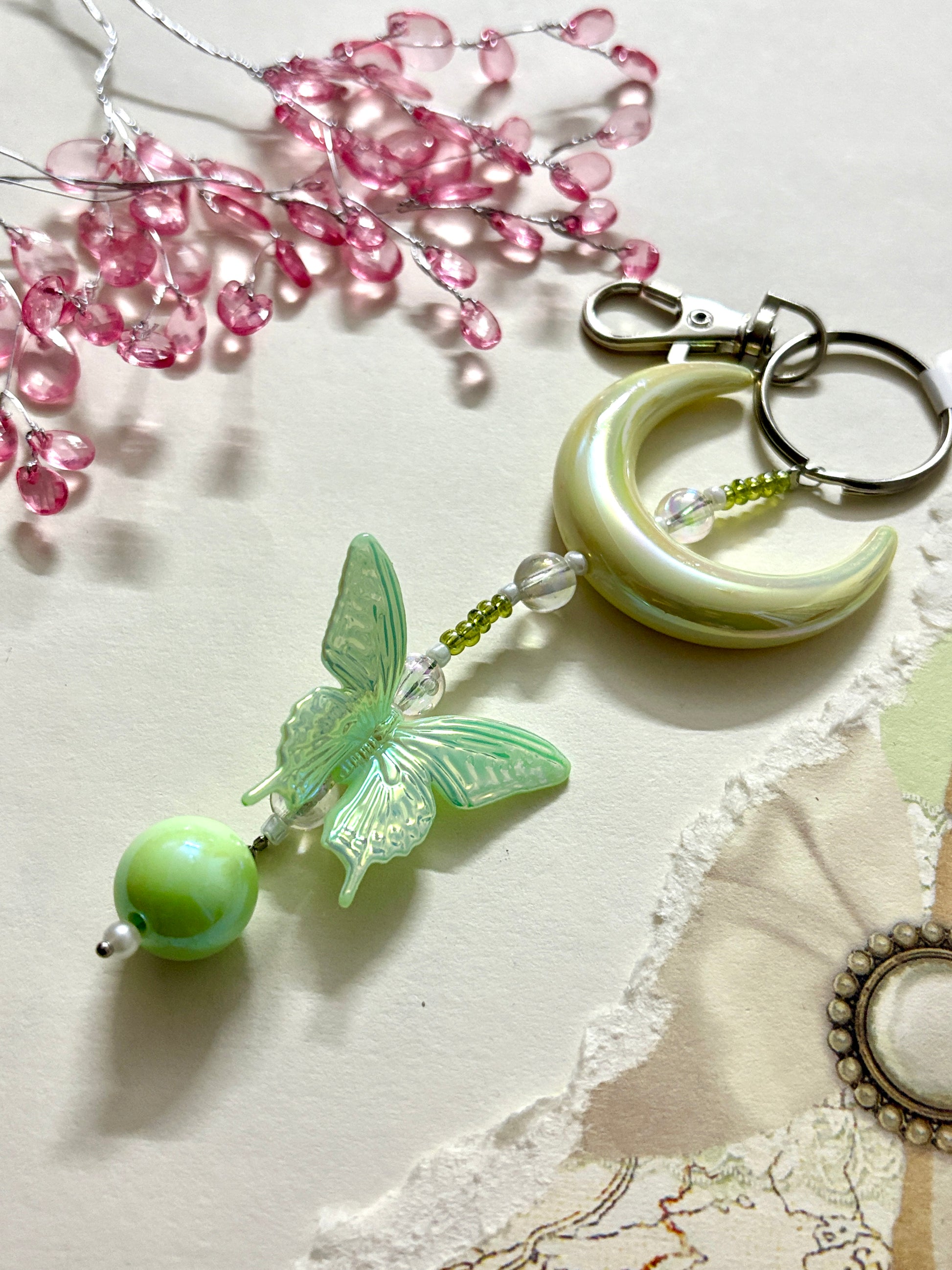 Elegant bag charm with moon, butterfly, and bead details hanging from a black leather handbag. Adds a whimsical and stylish touch to any bag.