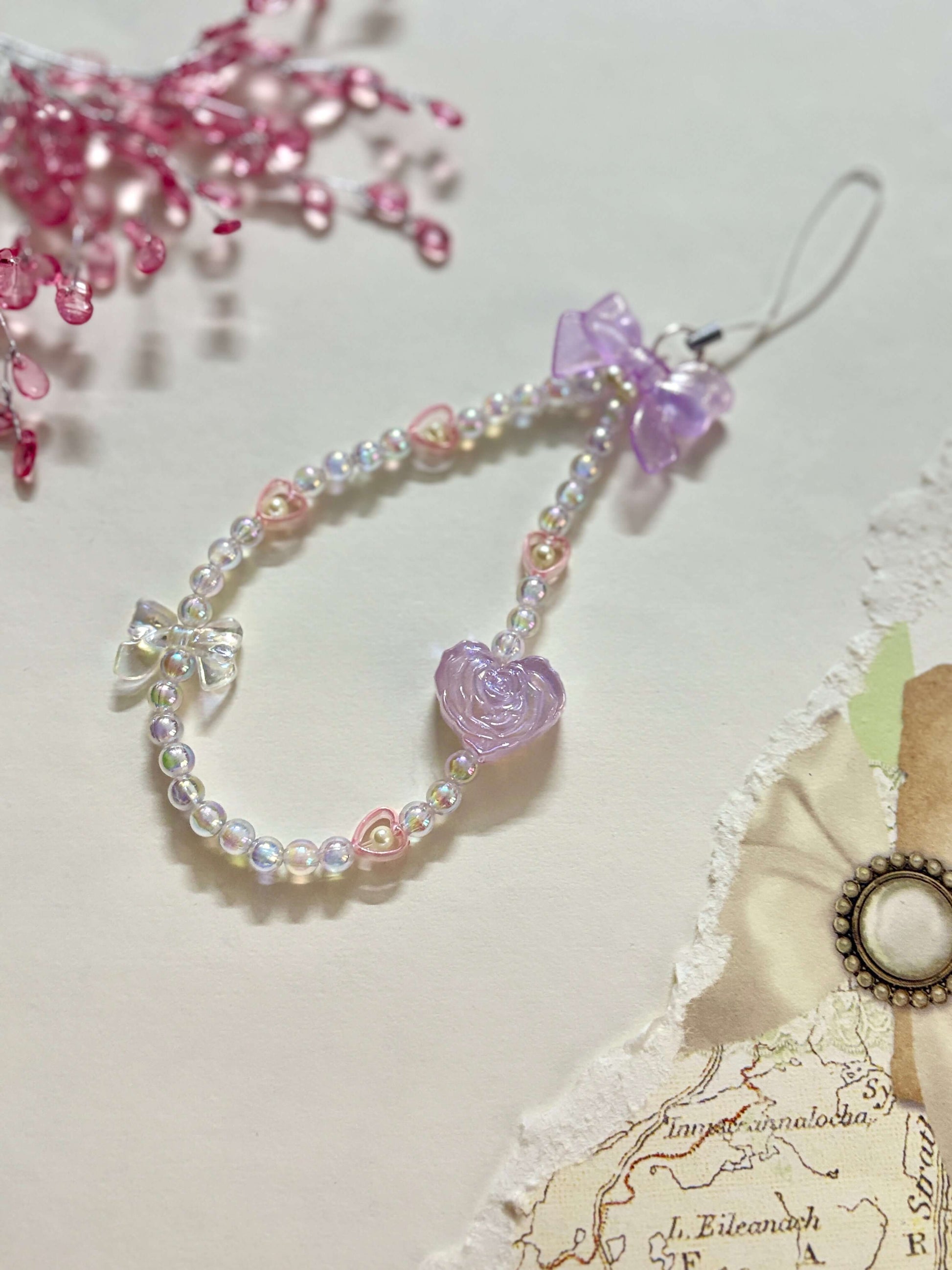 Beaded phone charm featuring a rose-shaped heart, delicate bow, and small heart accents; designed for attaching to mobile phones, adding a stylish and cute touch.