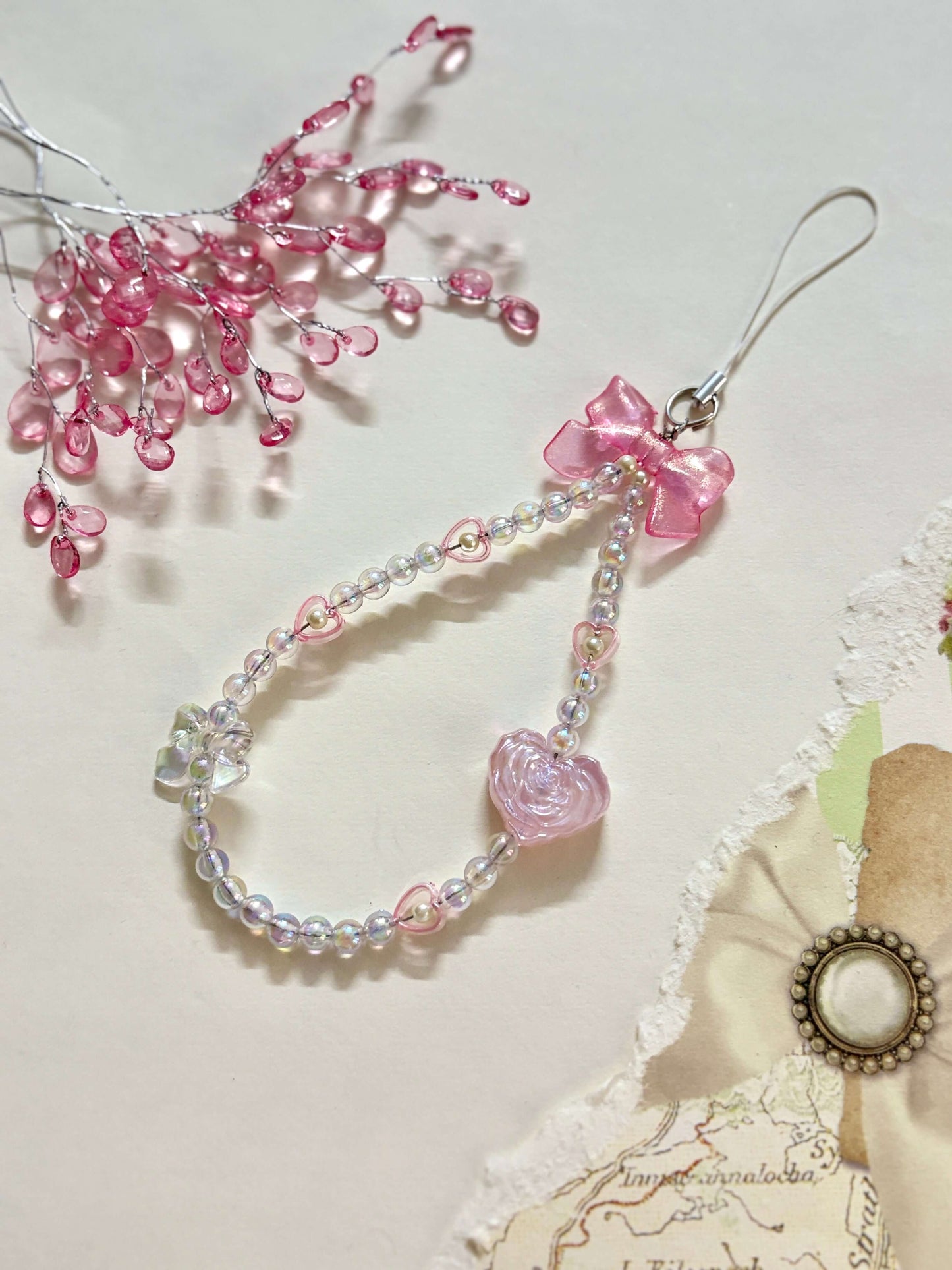 Beaded phone charm featuring a rose-shaped heart, delicate bow, and small heart accents; designed for attaching to mobile phones, adding a stylish and cute touch.