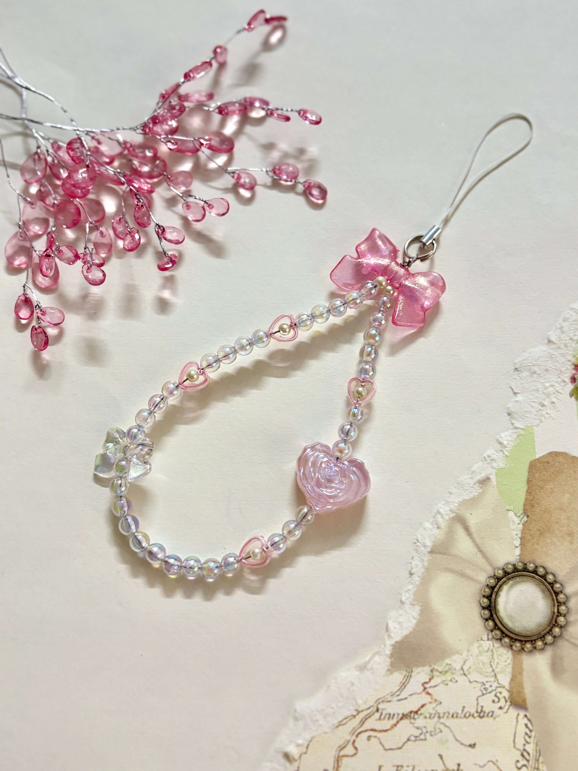 Beaded phone charm featuring a rose-shaped heart, delicate bow, and small heart accents; designed for attaching to mobile phones, adding a stylish and cute touch.