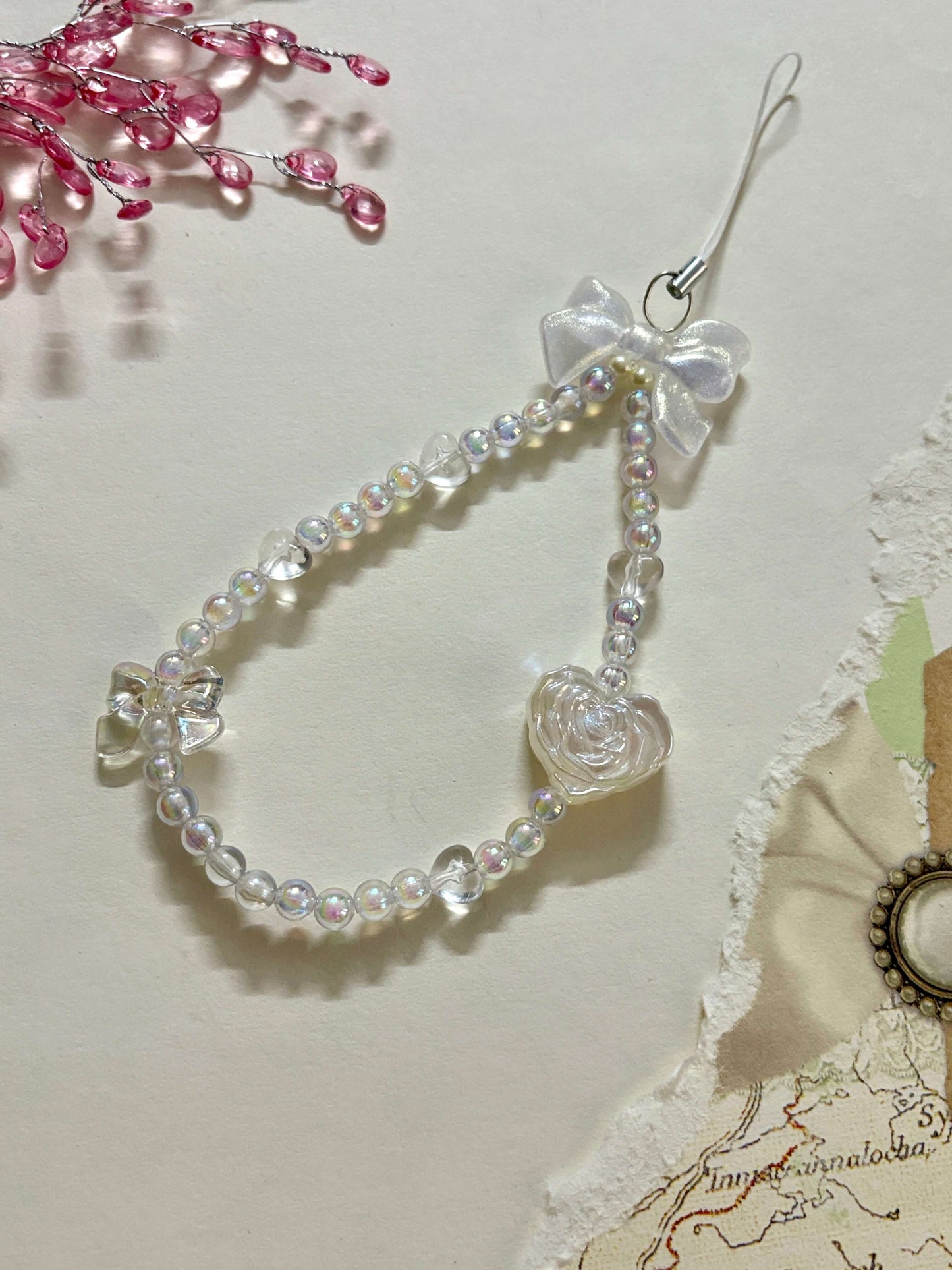 Beaded phone charm featuring a rose-shaped heart, delicate bow, and small heart accents; designed for attaching to mobile phones, adding a stylish and cute touch.