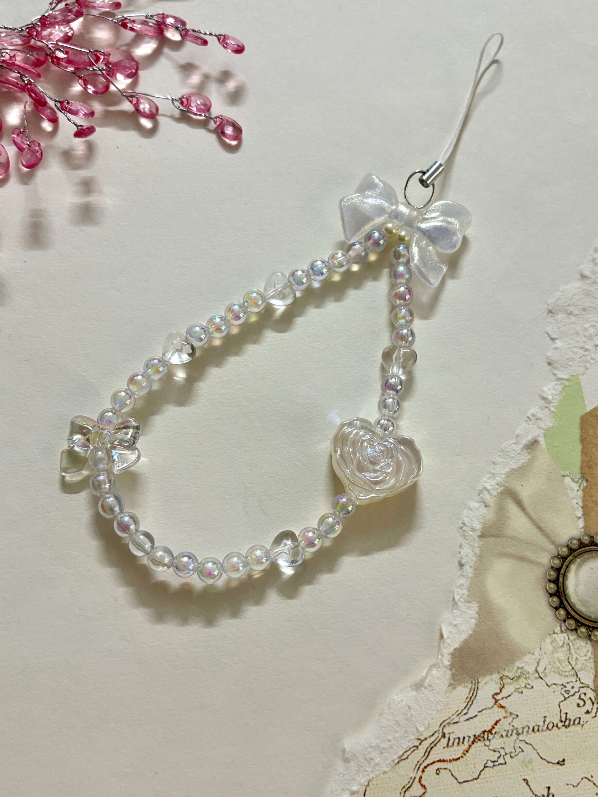 Beaded phone charm featuring a rose-shaped heart, delicate bow, and small heart accents; designed for attaching to mobile phones, adding a stylish and cute touch.
