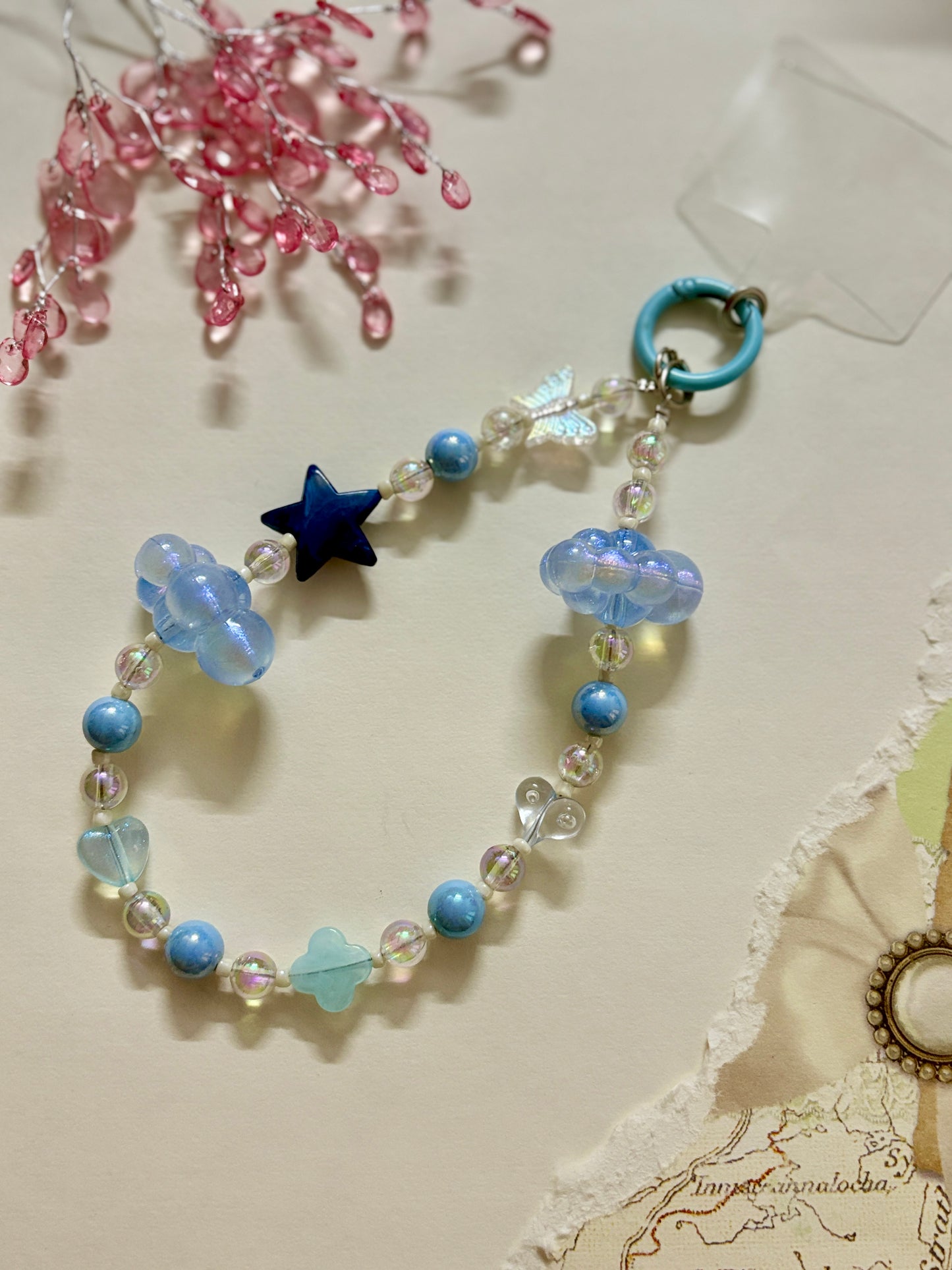 Aesthetic beaded phone charm featuring translucent clouds, a navy star, pastel beads, and butterfly accents, arranged in a dreamy celestial theme.