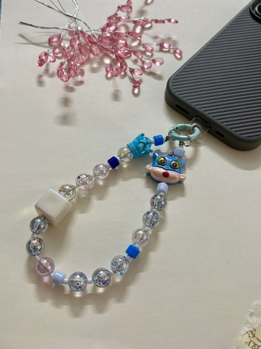 A handmade phone charm strap featuring glitter-filled resin beads, blue and white accents, a Shin Chan character charm, and a secure loop for attaching to phone cases or bags.
