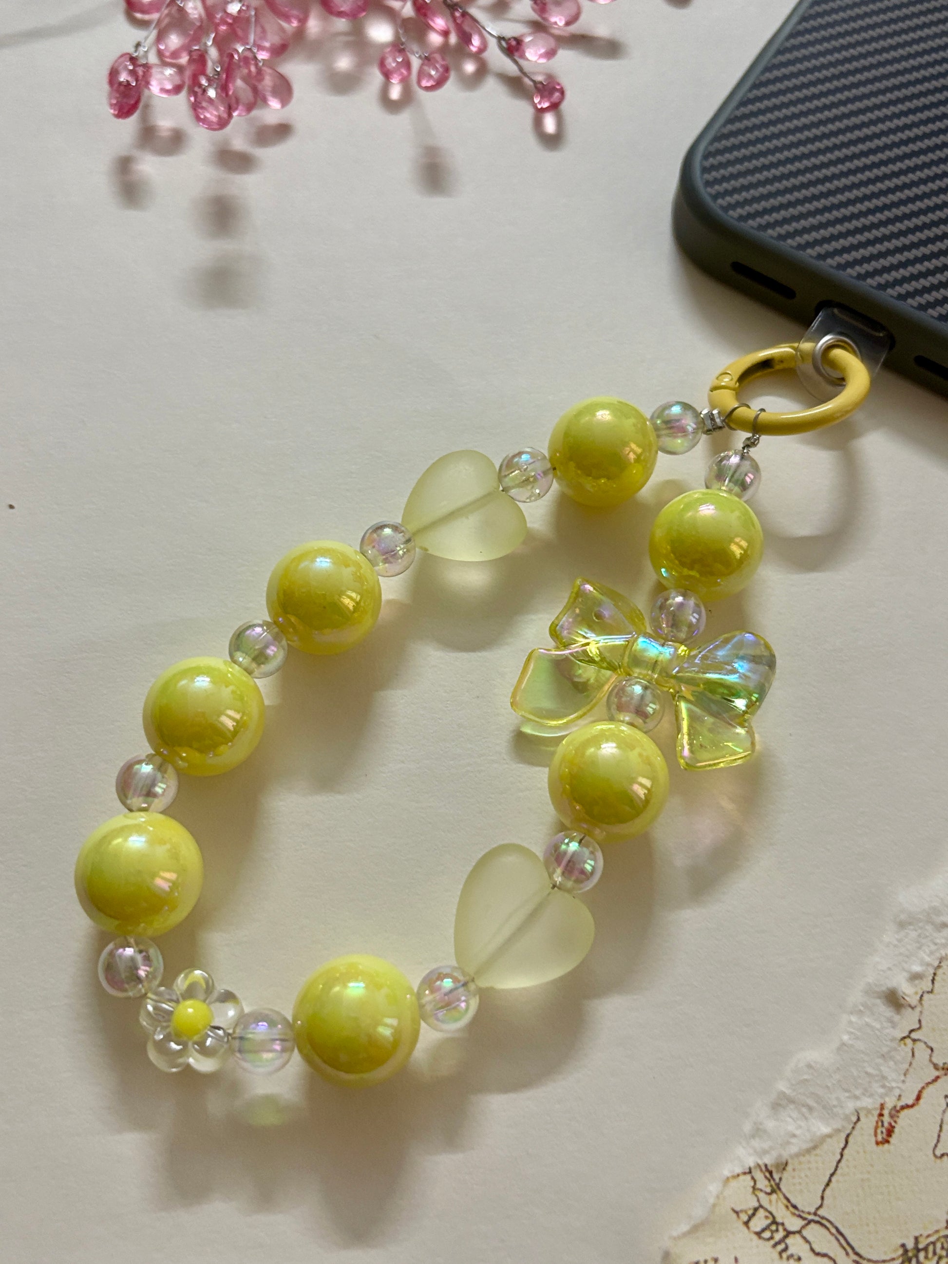 A cute phone charm made with glossy and translucent beads in various shapes, including a bow accent, strung together on an elastic loop with a plastic strap attachment.