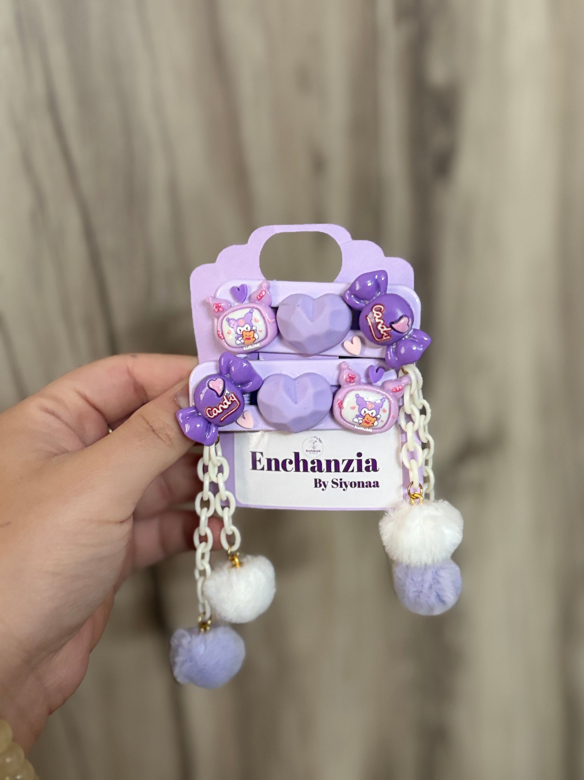 Set of purple kawaii Kuromi hair clips with heart, candy, and Kuromi designs. Decorated with chains and fluffy pom-poms. Fun accessory from Enchanzia by Siyonaa.