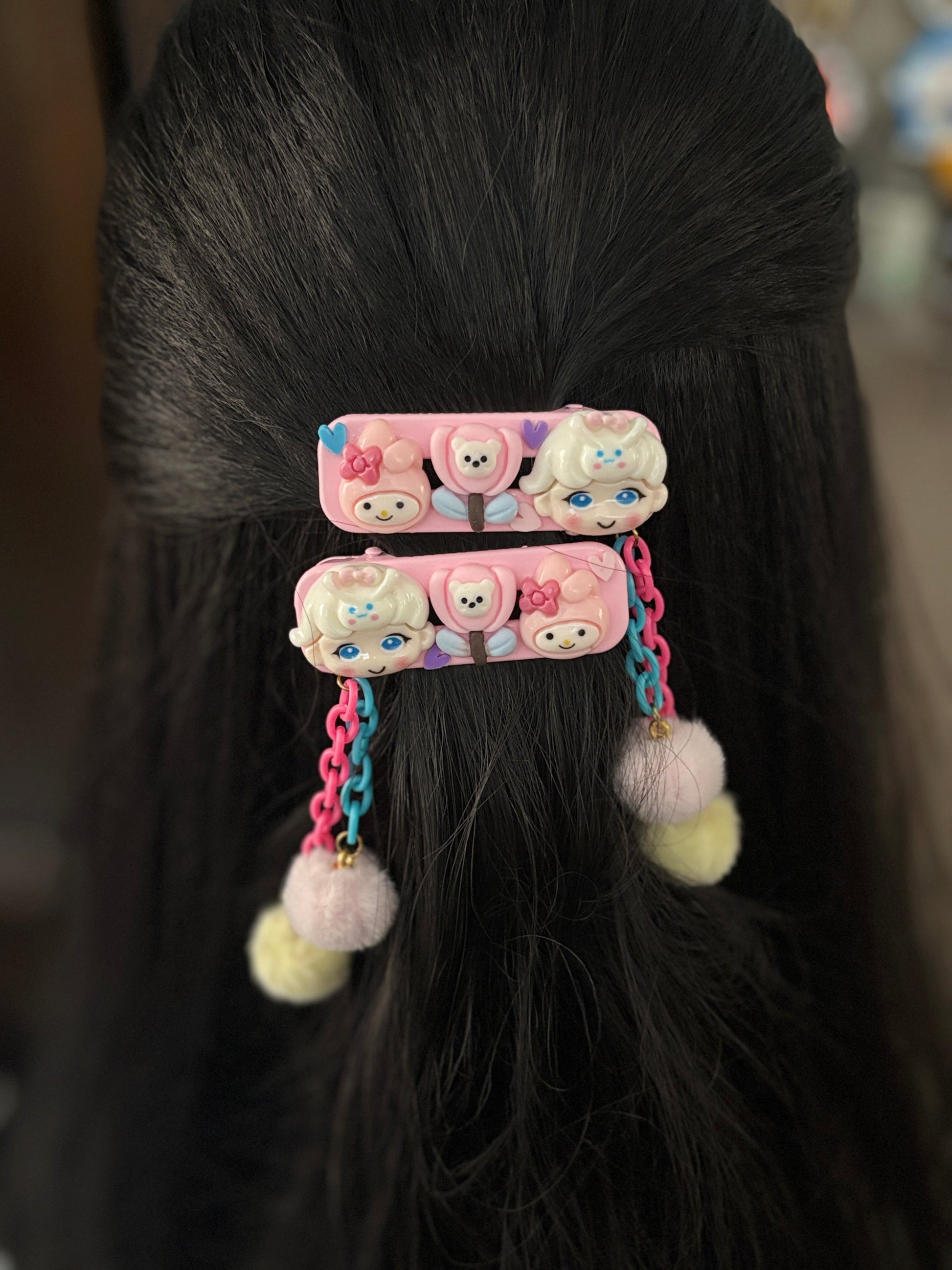 Set of My Melody-themed hair clips with pink and blue chains, fuzzy pom pom dangles, and cute cartoon faces—ideal for playful, fun hairstyles for kids.
