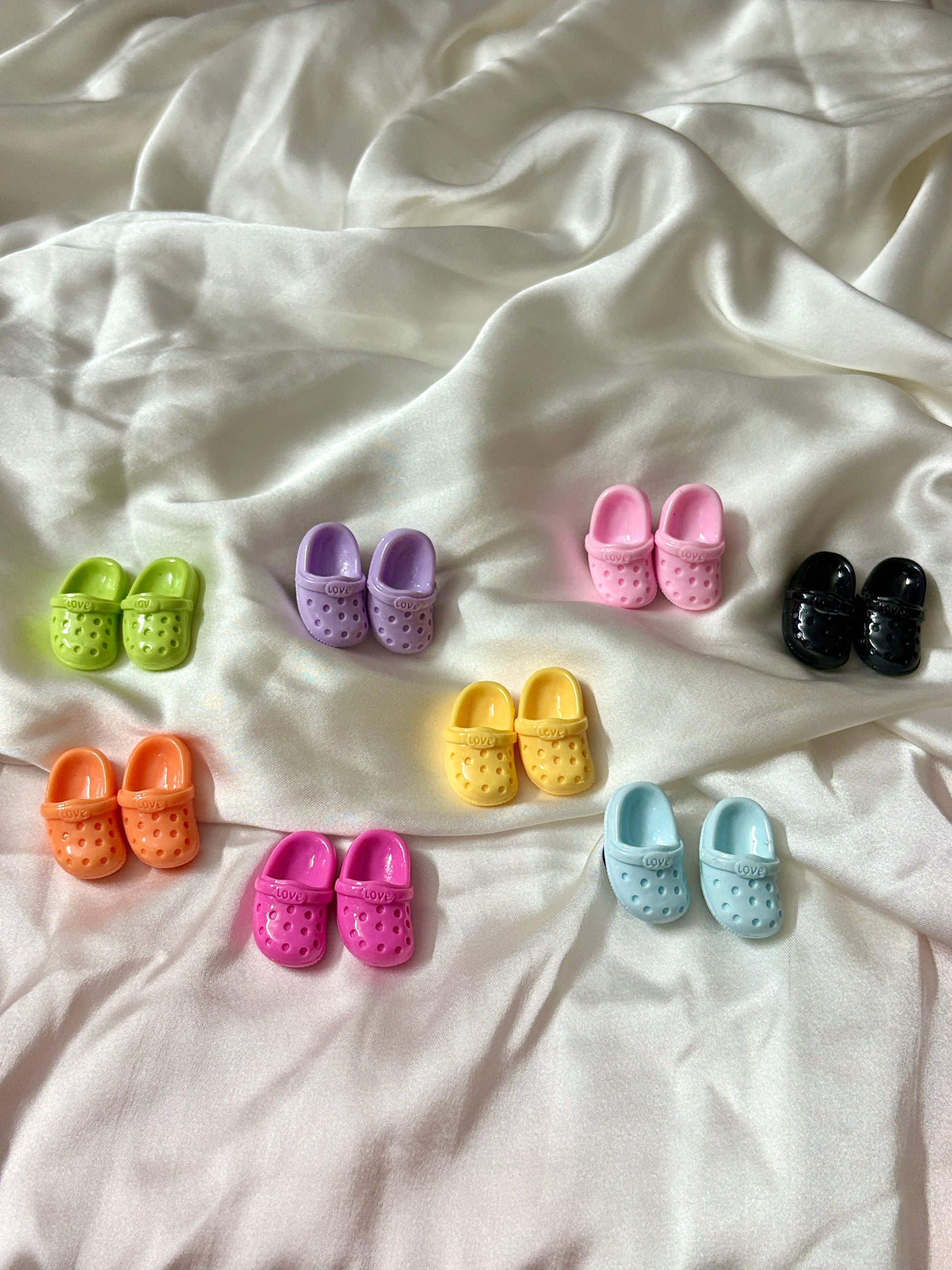 Colorful Crocs-shaped Jibbitz charms in matching pairs, with vibrant shades like pink, blue, yellow, black, and more—perfect for a quirky Crocs upgrade.
