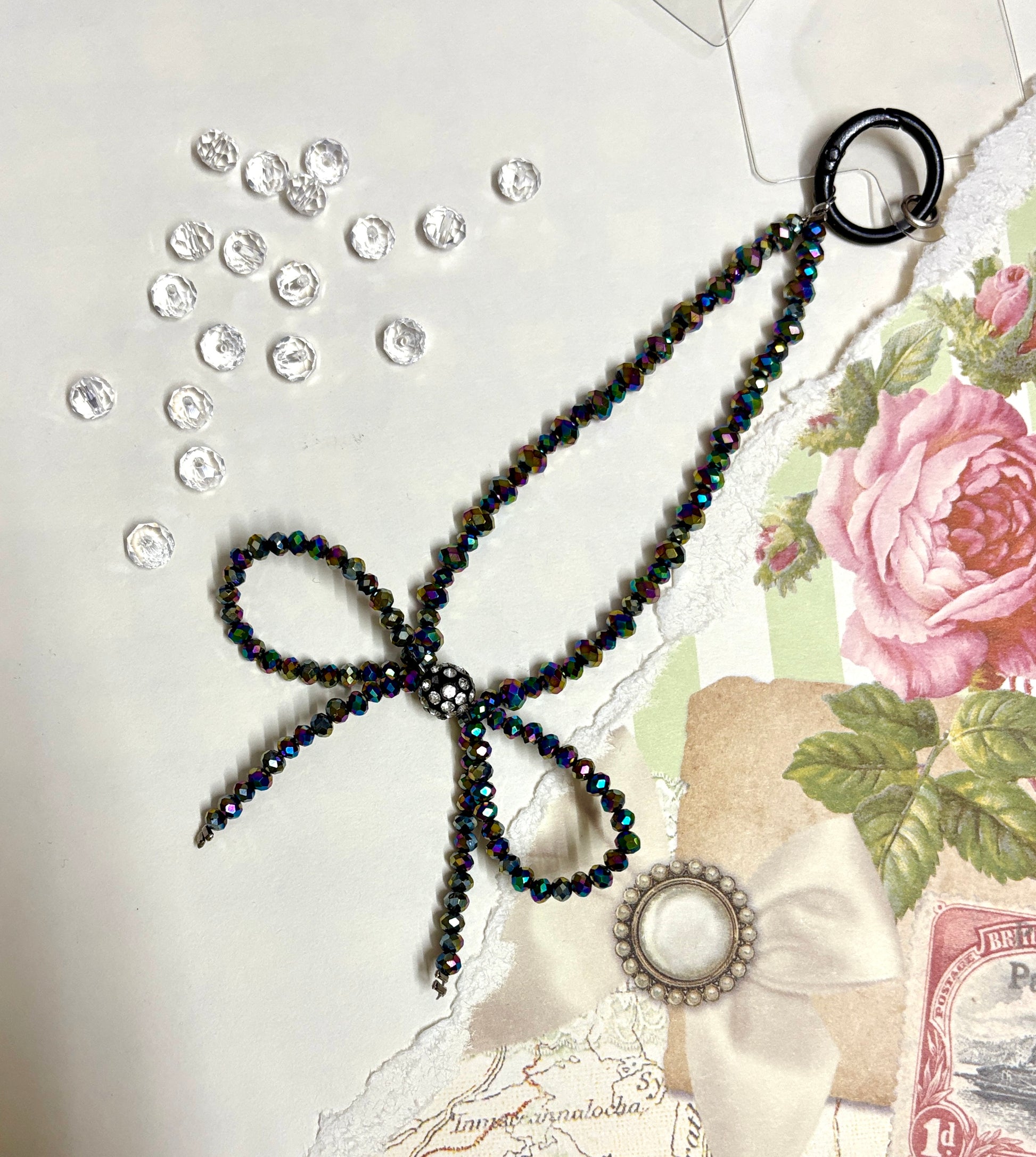 Elegant beaded phone charm featuring a delicate crystal bow design with faceted beads and a rhinestone center, styled with vintage floral paper.