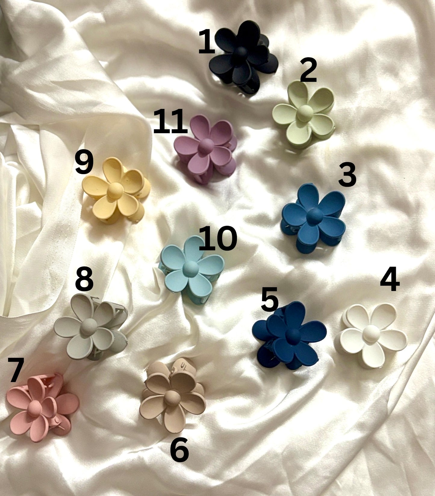 Top view of 11 colorful matte mini flower claw clips arranged on white satin, featuring soft pastel tones, ideal for cute, minimal hair styling for women & girls.
