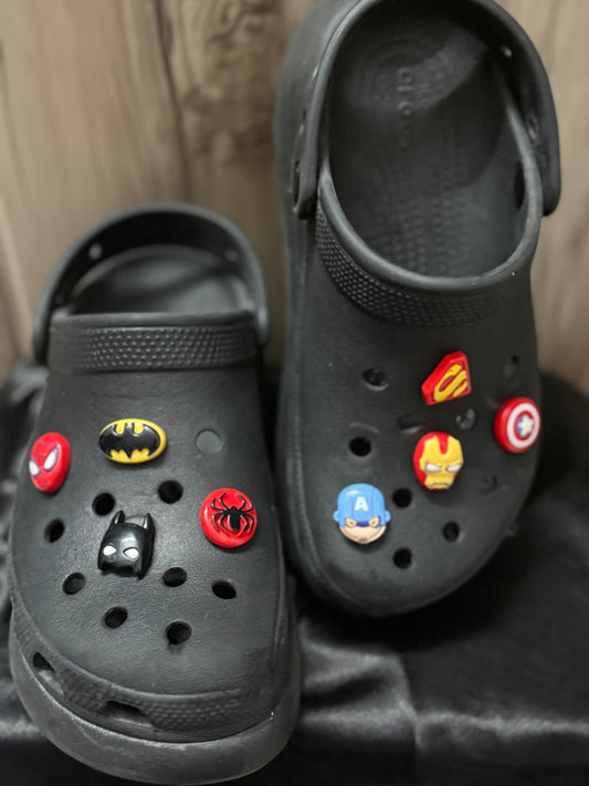 Black Crocs decorated with superhero-themed Jibbitz charms including Spider-Man, Iron Man, Captain America, Batman, and Superman icons.
