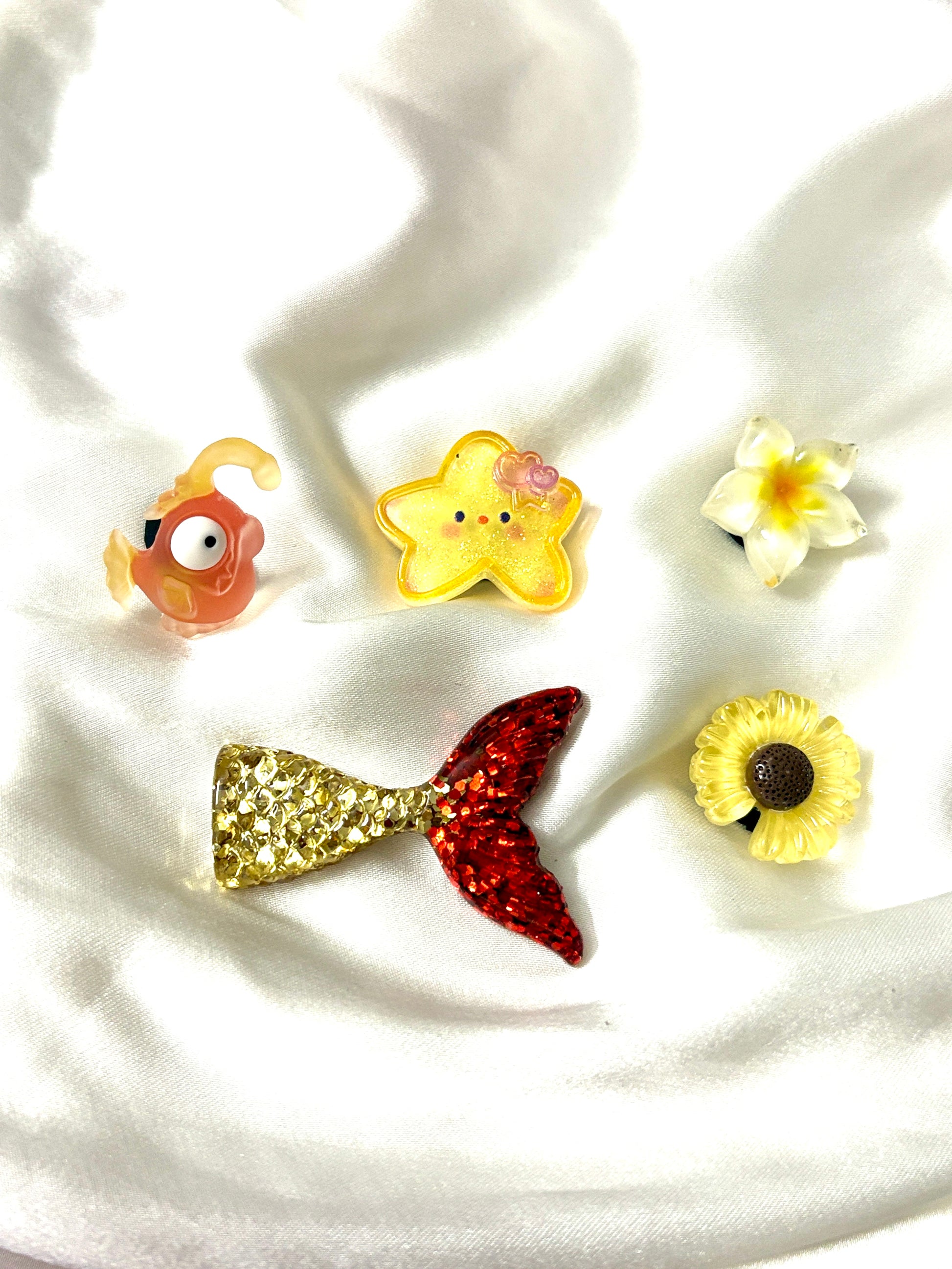 Set of 5 tropical-themed Crocs Jibbitz charms featuring a glitter mermaid tail, yellow starfish, tropical flowers, and an orange cartoon fish.