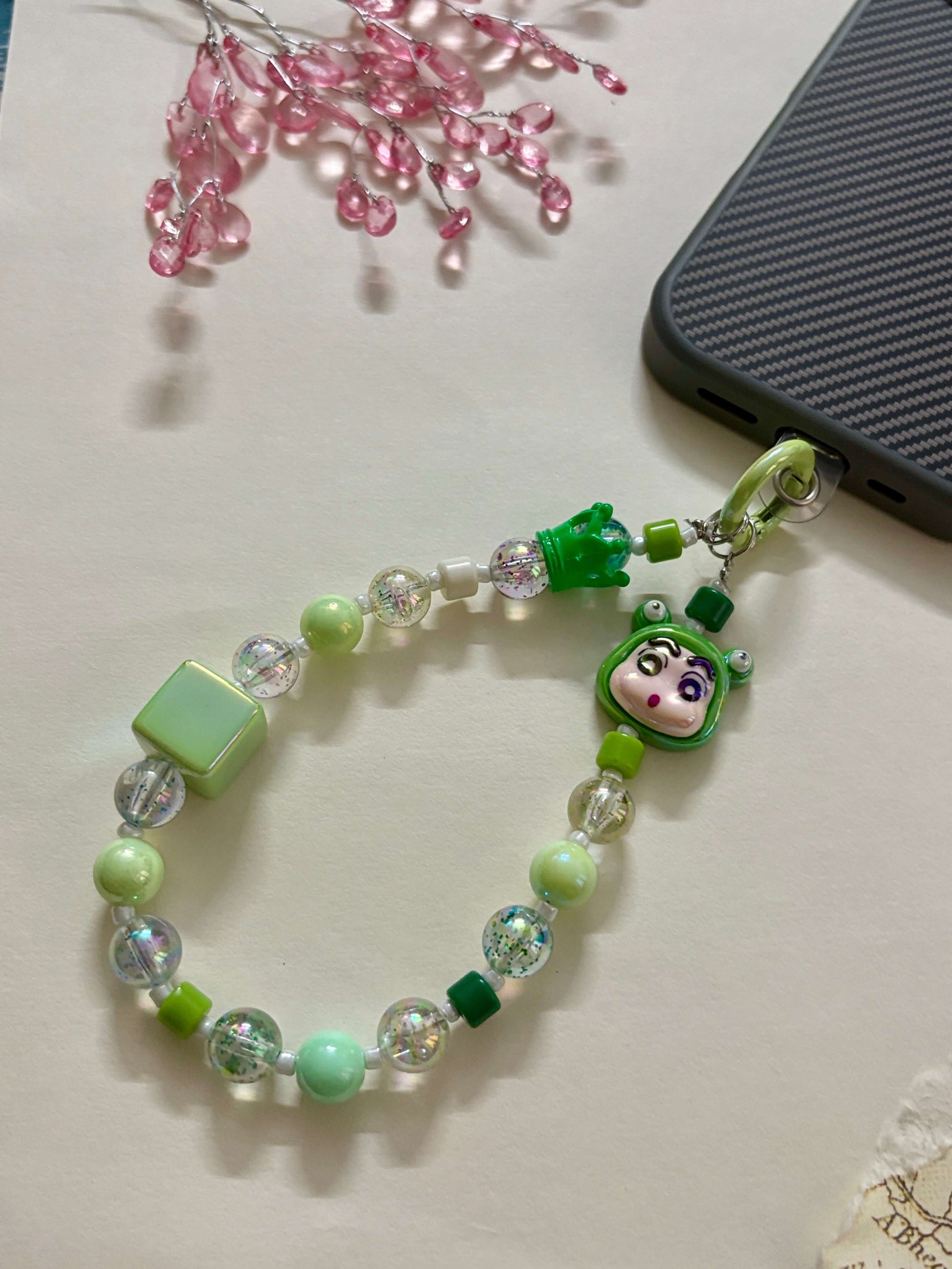 A handmade phone charm strap featuring glitter-filled resin beads, blue and white accents, a Shin Chan character charm, and a secure loop for attaching to phone cases or bags.
