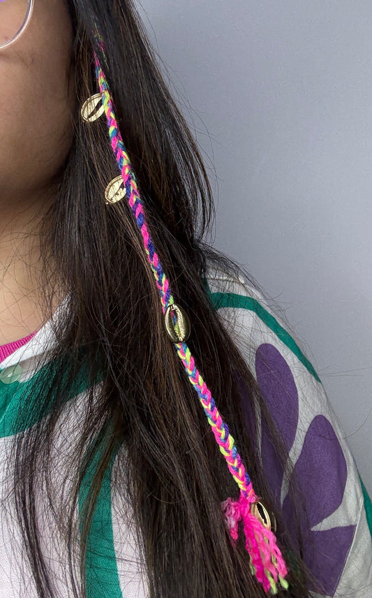 A vibrant neon-colored Goa-style hair braid featuring braided threads in bright pink, yellow, and blue, decorated with metallic cowrie shells and styled into natural hair for a fun, beachy look.