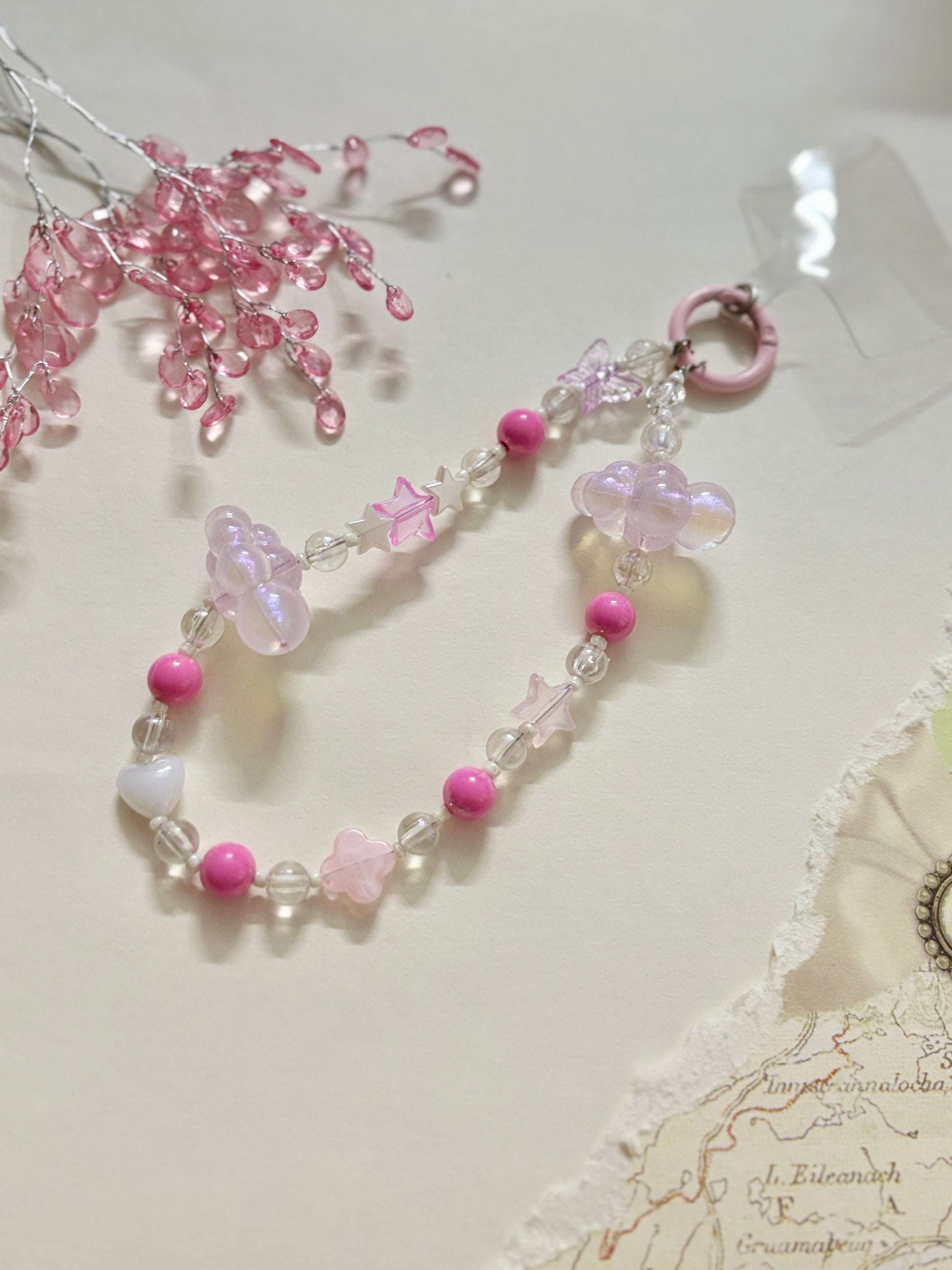 Aesthetic beaded phone charm featuring translucent clouds, a navy star, pastel beads, and butterfly accents, arranged in a dreamy celestial theme.