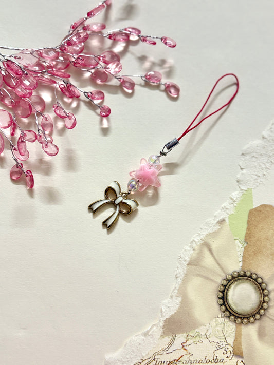 Cute phone charm featuring a star bead, enamel bow charm, and iridescent beads, styled with soft floral decor and a delicate strap.