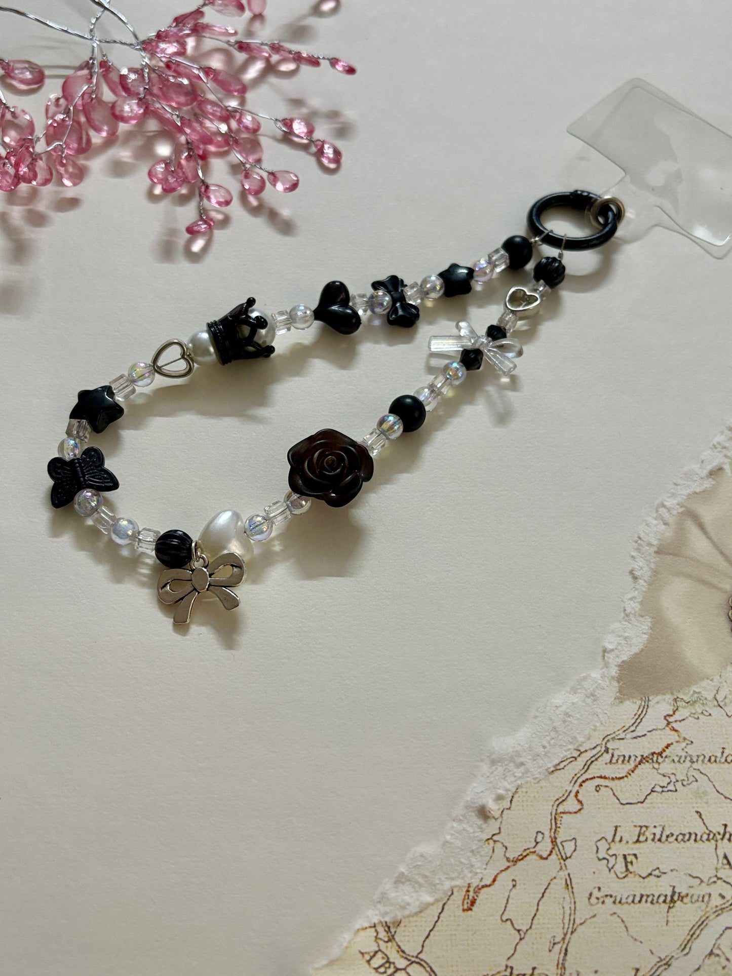 
“Handmade black and white beaded phone charm with rose, heart, bow, and butterfly charms in kawaii aesthetic”