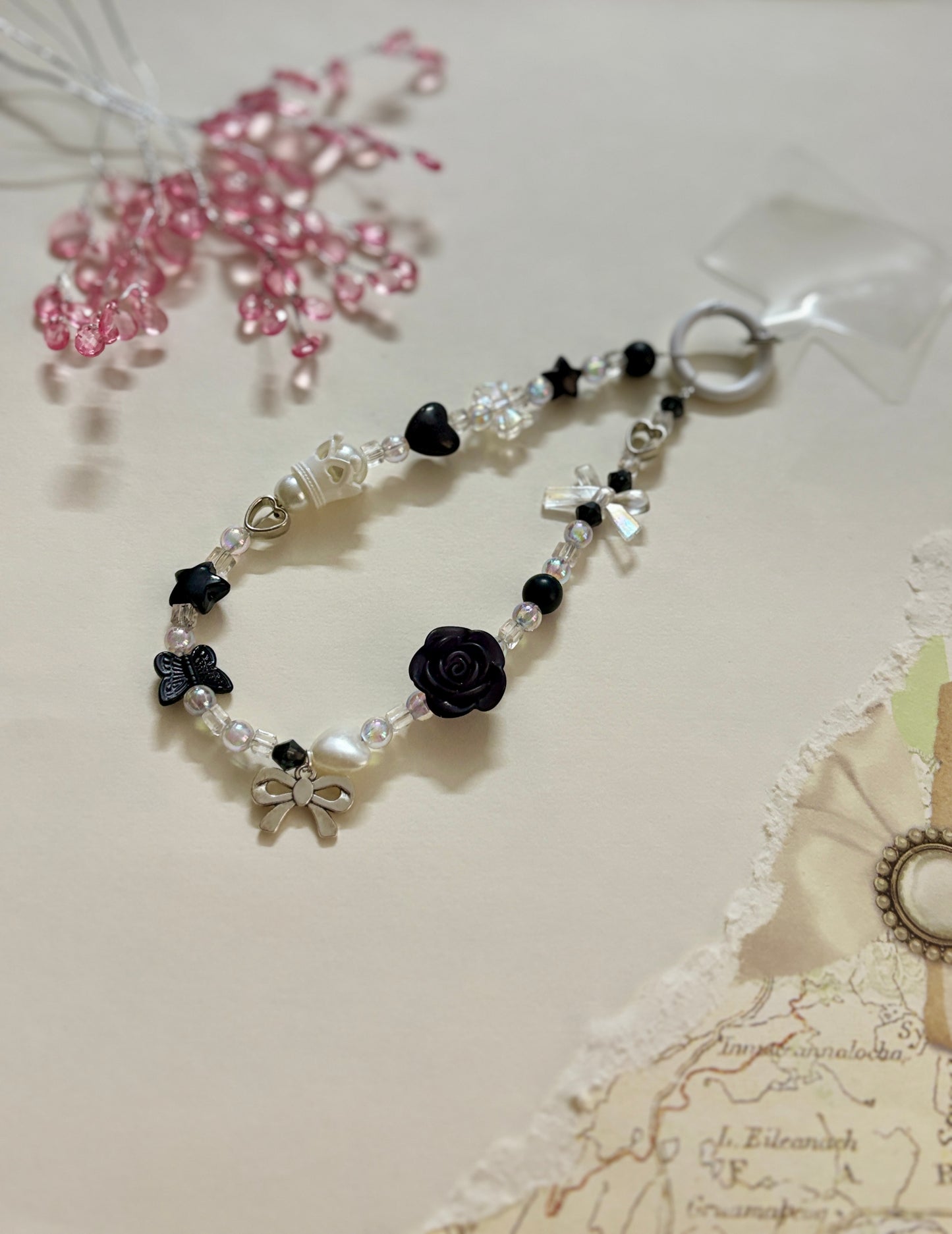 
“Handmade black and white beaded phone charm with rose, heart, bow, and butterfly charms in kawaii aesthetic”