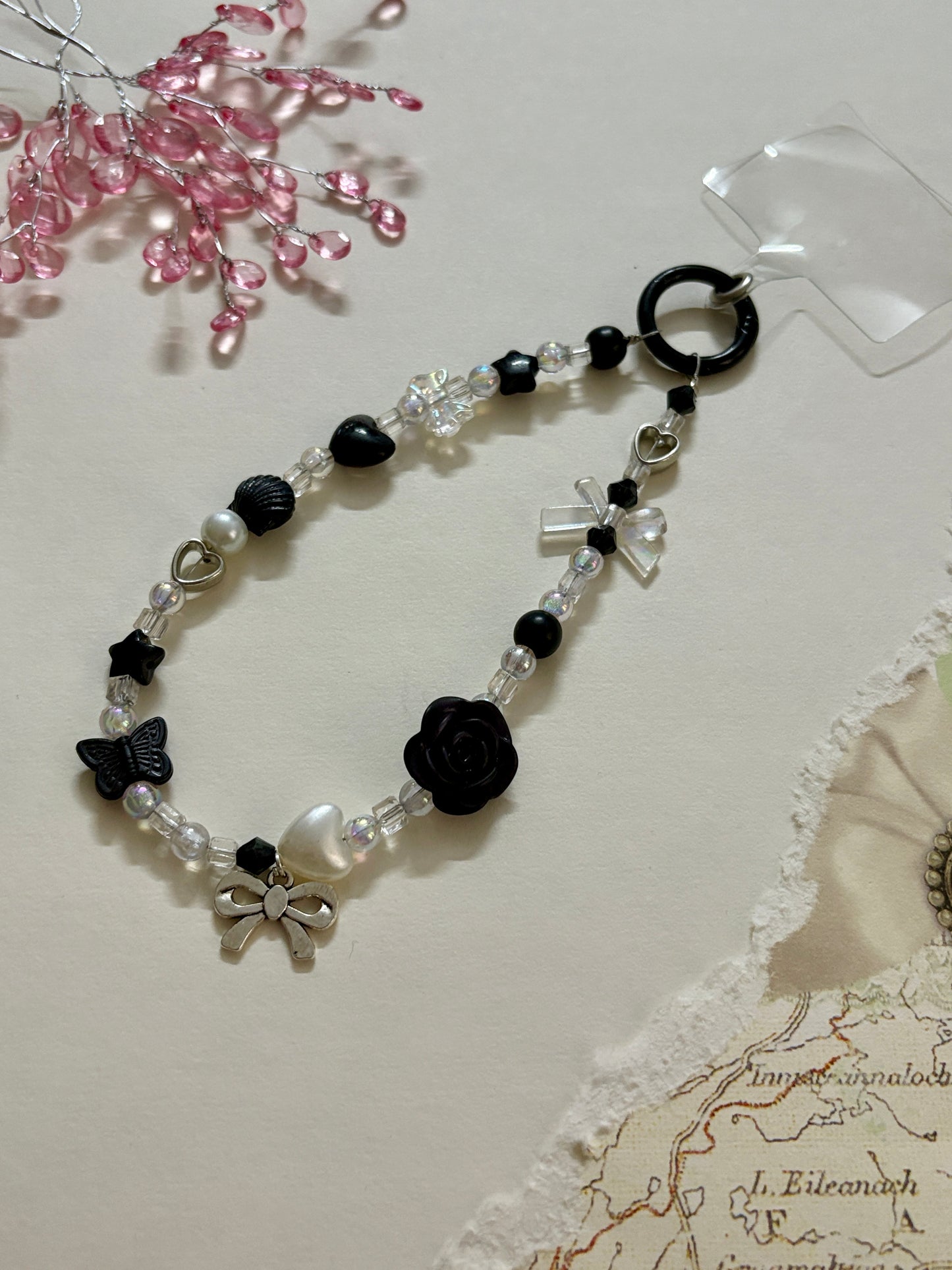 
“Handmade black and white beaded phone charm with rose, heart, bow, and butterfly charms in kawaii aesthetic”