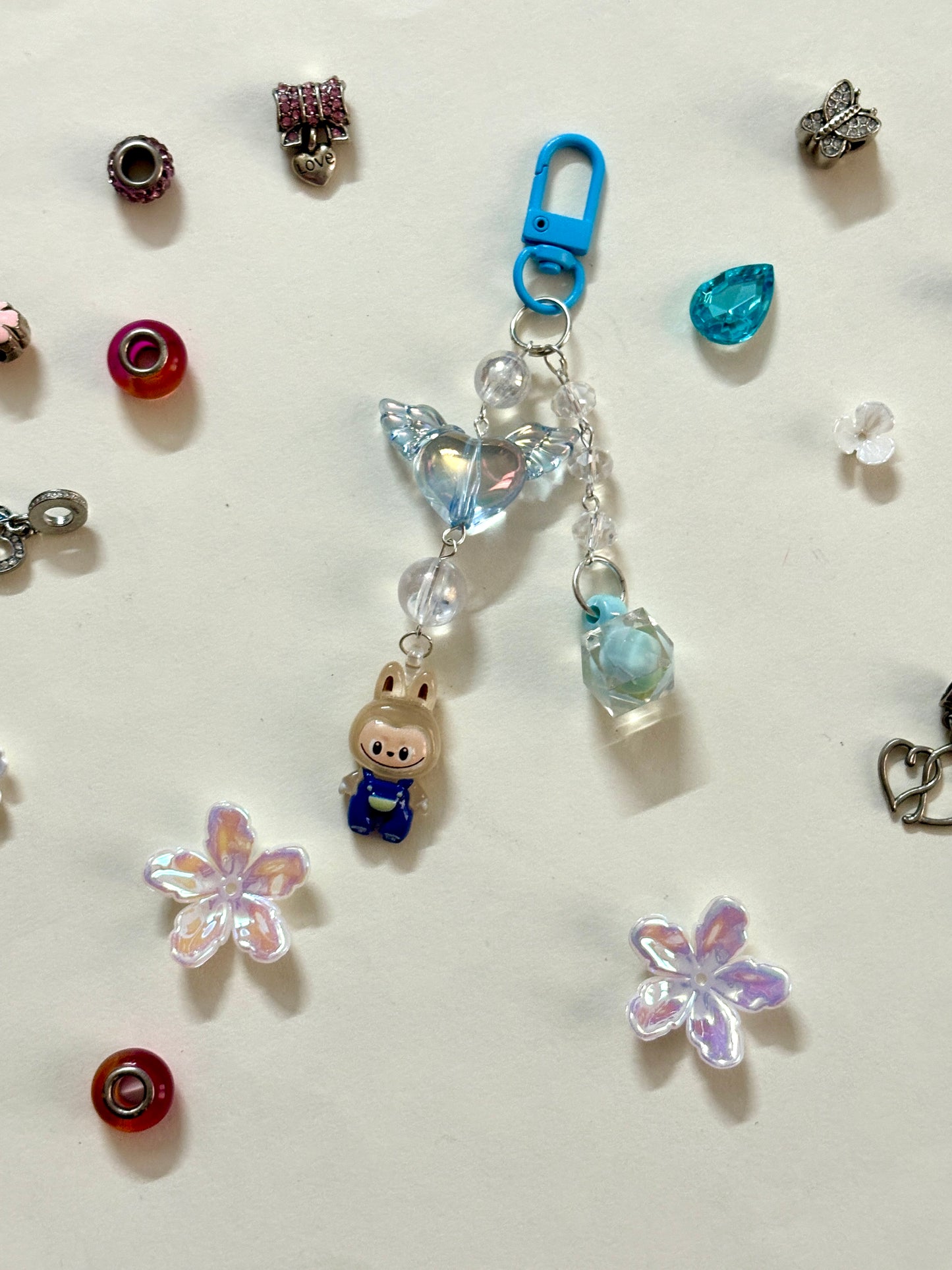 Labubu bag charm featuring a blue-outfitted figure, crystal beads, and pastel clip — a rare and playful accessory available in 2 colors, attached to a black bag.
