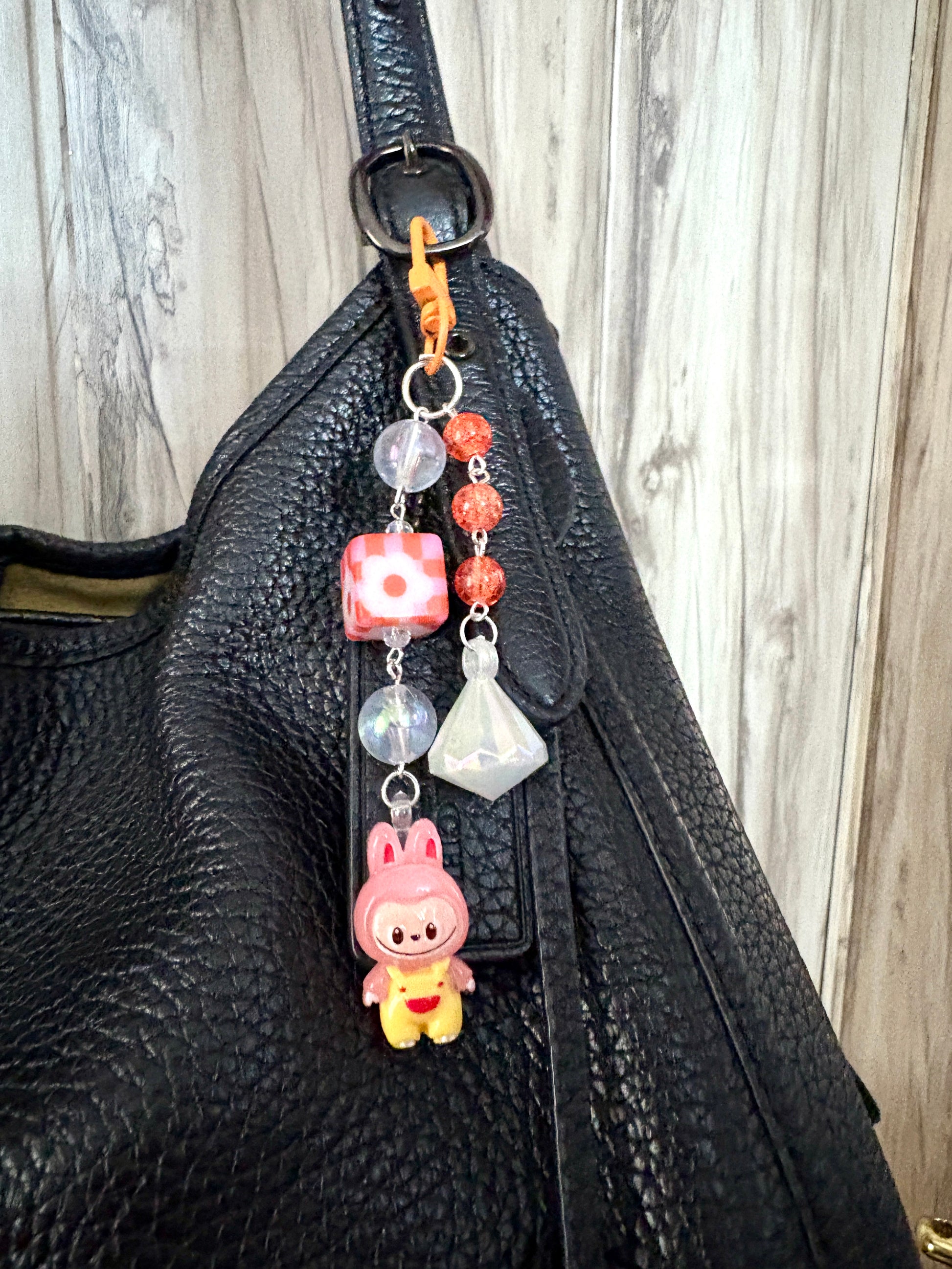 Labubu bag charm featuring a blue-outfitted figure, crystal beads, and pastel clip — a rare and playful accessory available in 2 colors, attached to a black bag.
