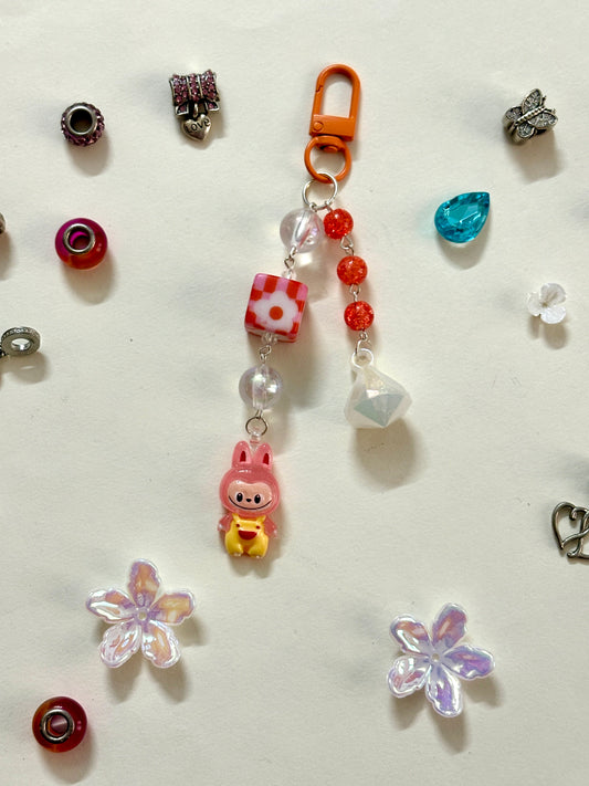 Labubu bag charm featuring a blue-outfitted figure, crystal beads, and pastel clip — a rare and playful accessory available in 2 colors, attached to a black bag.
