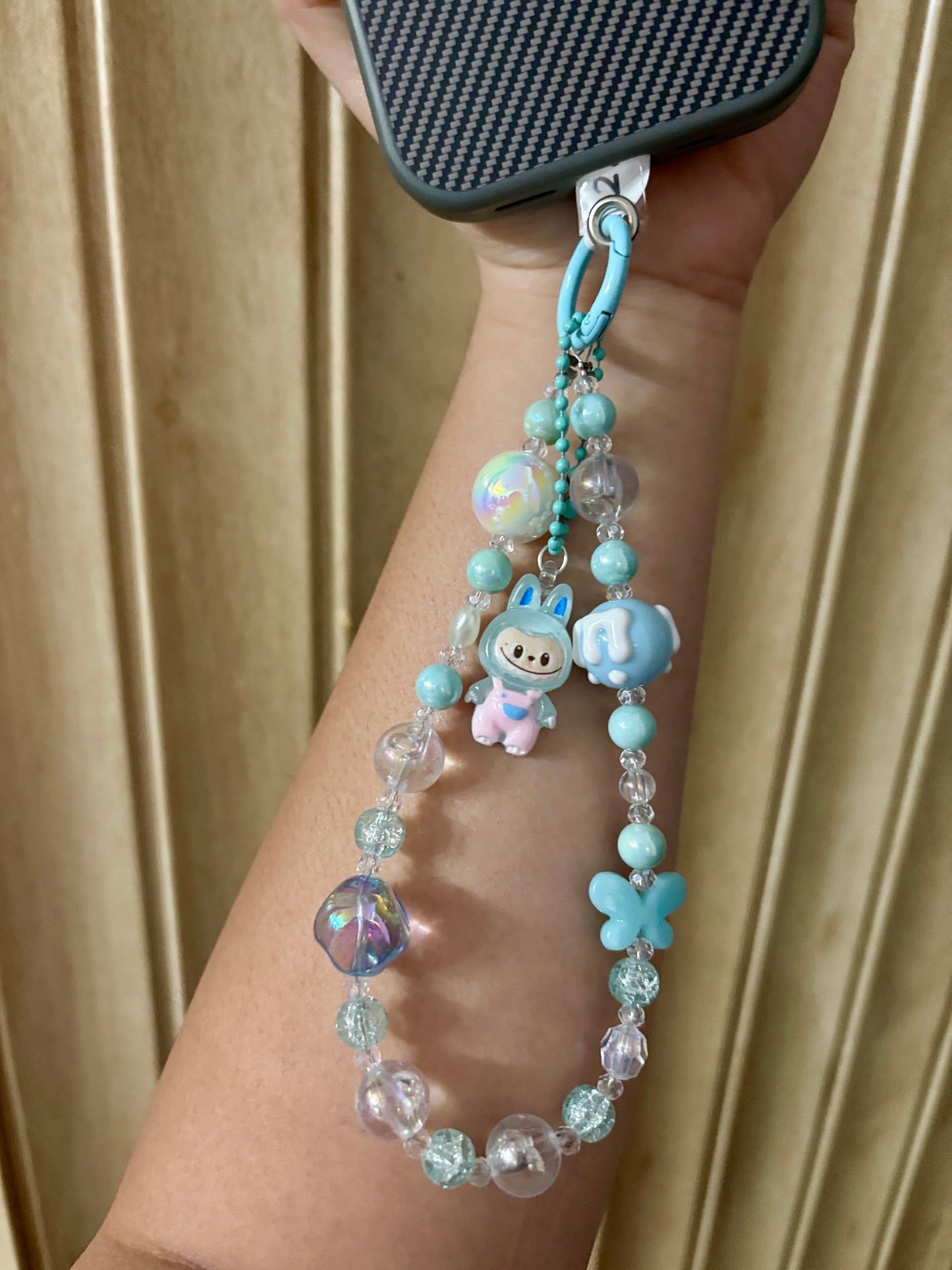 Close-up of a pink Labubu phone charm strap featuring clear and glitter beads, butterfly detail, and the rare Labubu figure — now available in three colors.