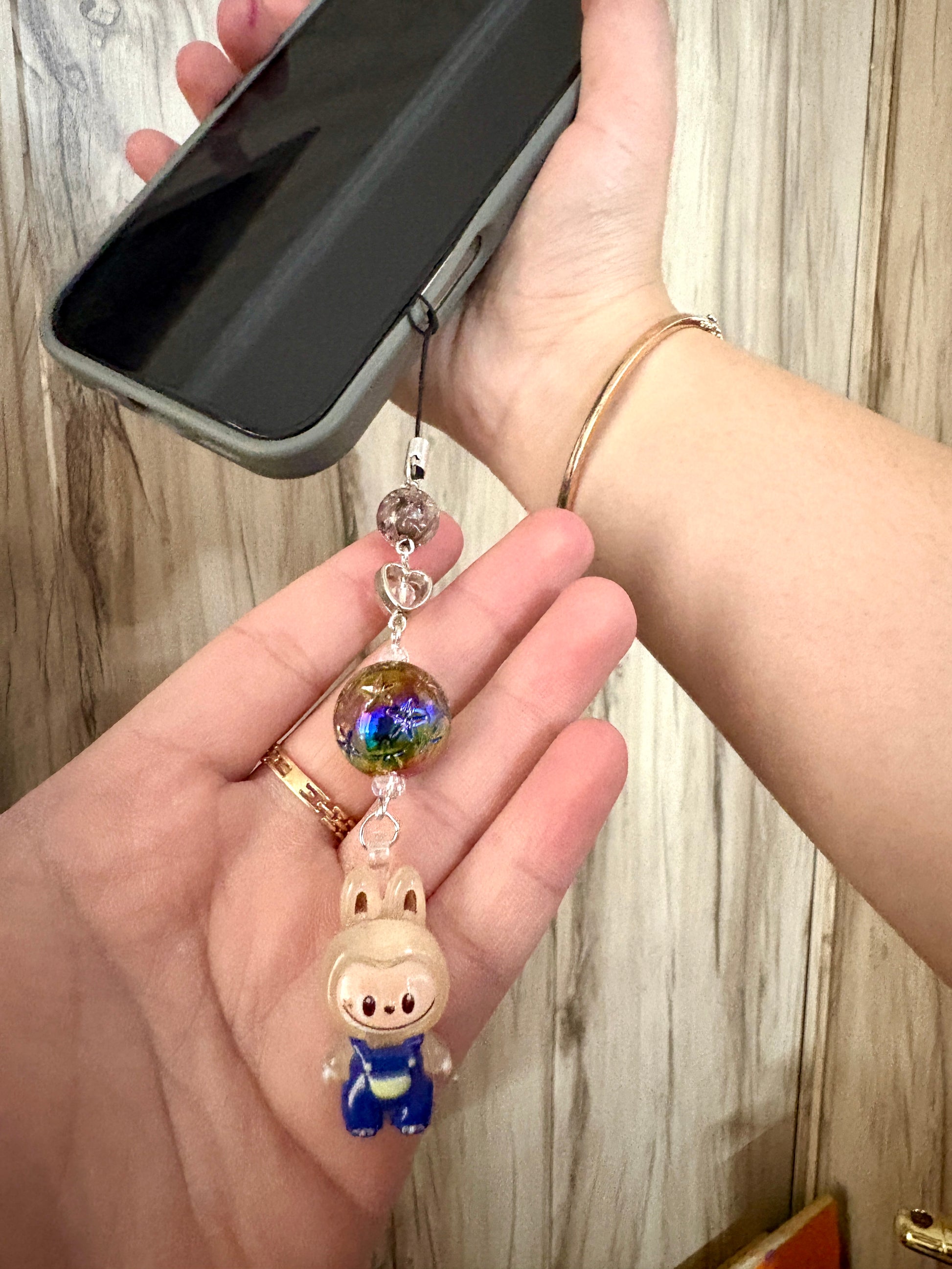 Mini Labubu phone charm with rainbow orb bead and black strap, featuring Labubu in blue overalls — collectible strap available in two color options.