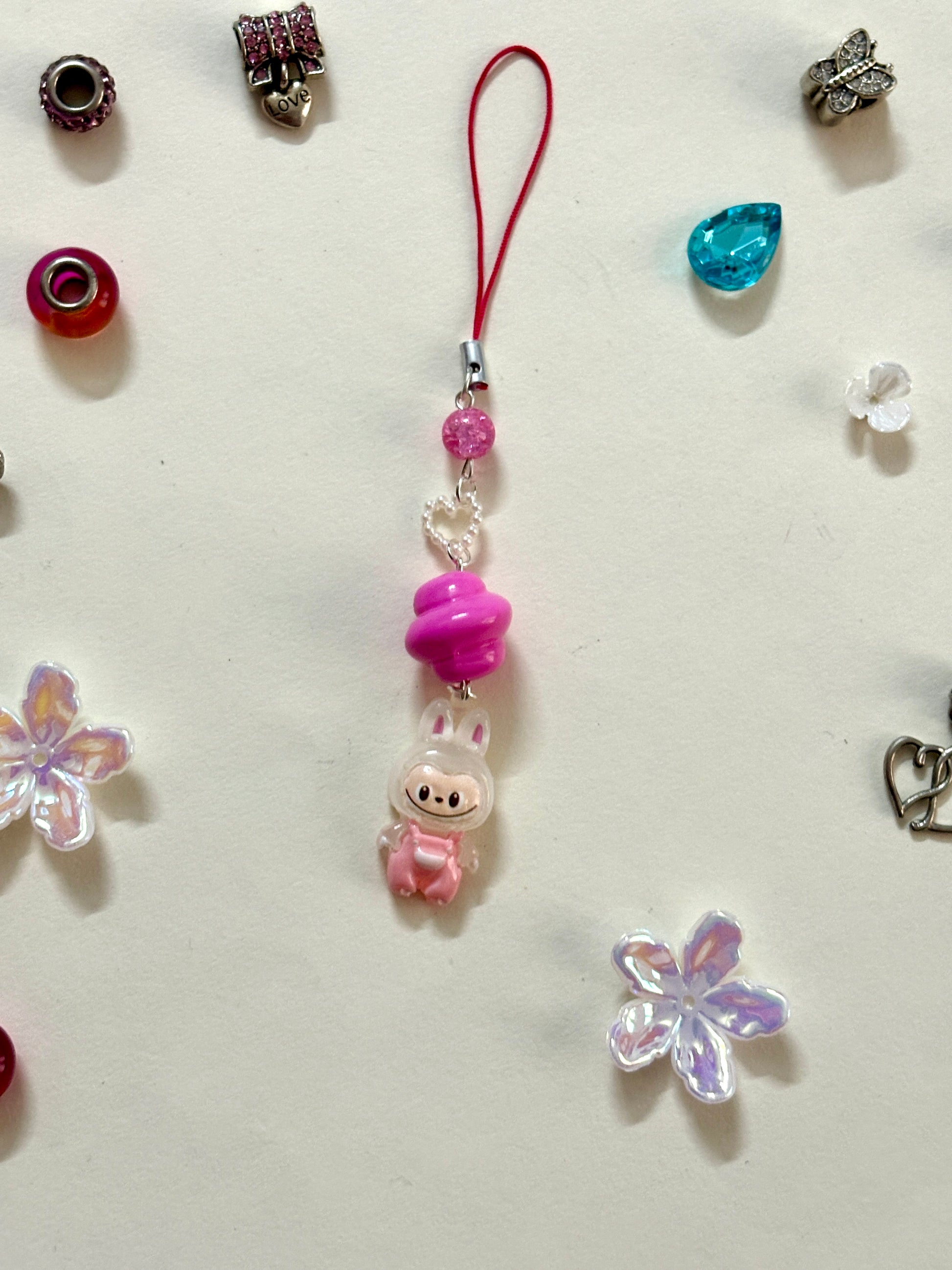 Mini Labubu phone charm with rainbow orb bead and black strap, featuring Labubu in blue overalls — collectible strap available in two color options.