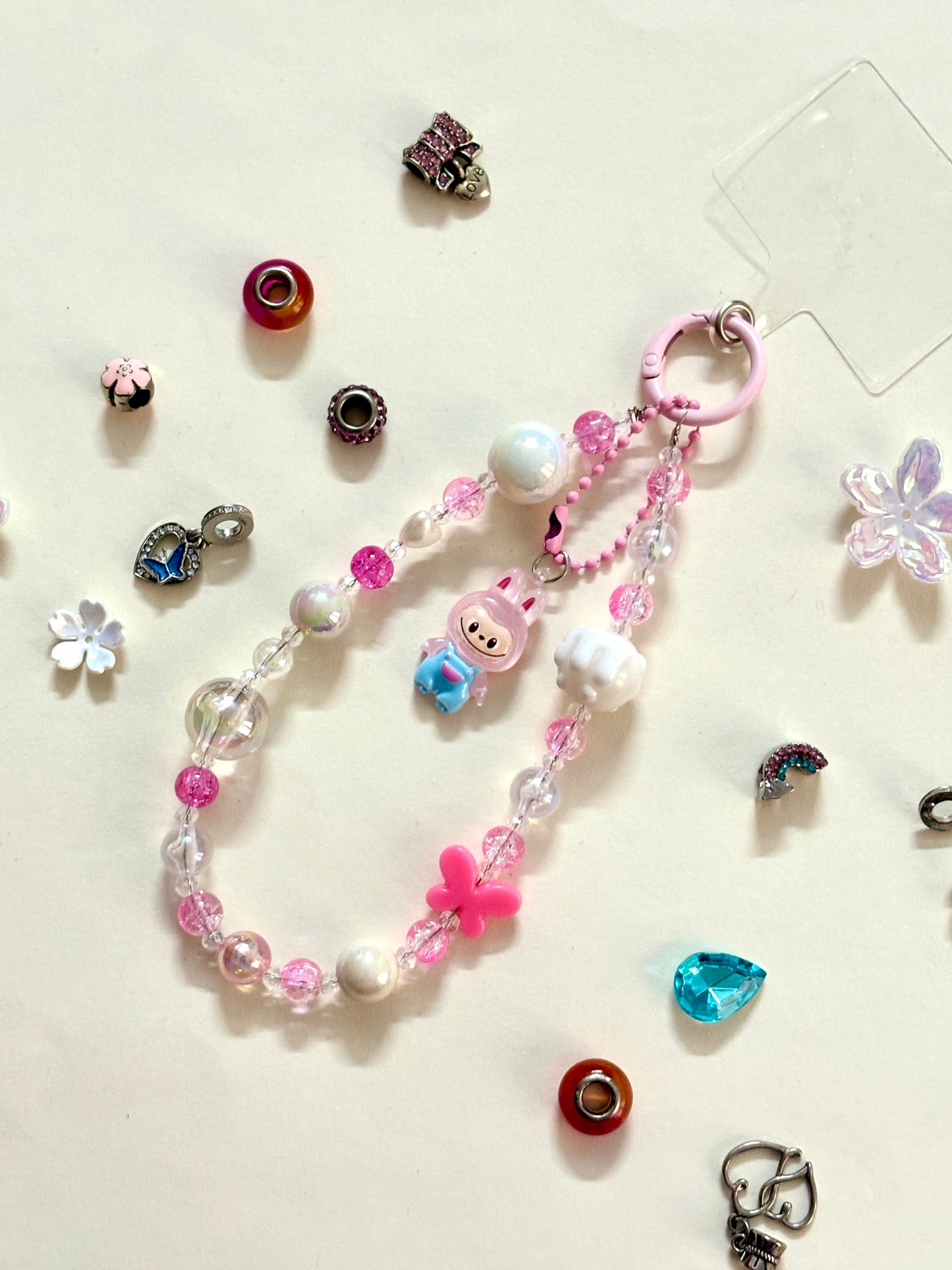 Close-up of a pink Labubu phone charm strap featuring clear and glitter beads, butterfly detail, and the rare Labubu figure — now available in three colors.