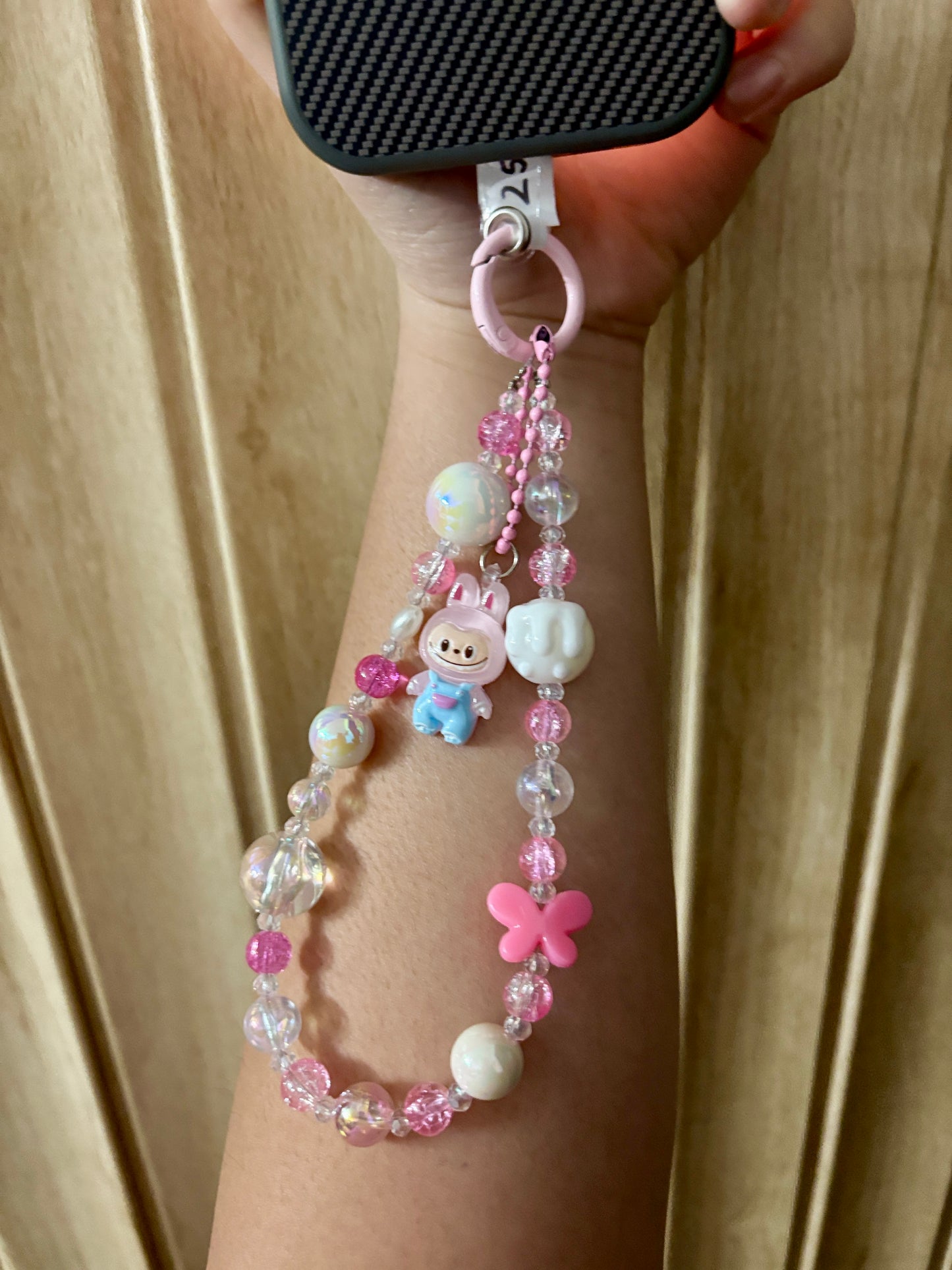 Close-up of a pink Labubu phone charm strap featuring clear and glitter beads, butterfly detail, and the rare Labubu figure — now available in three colors.