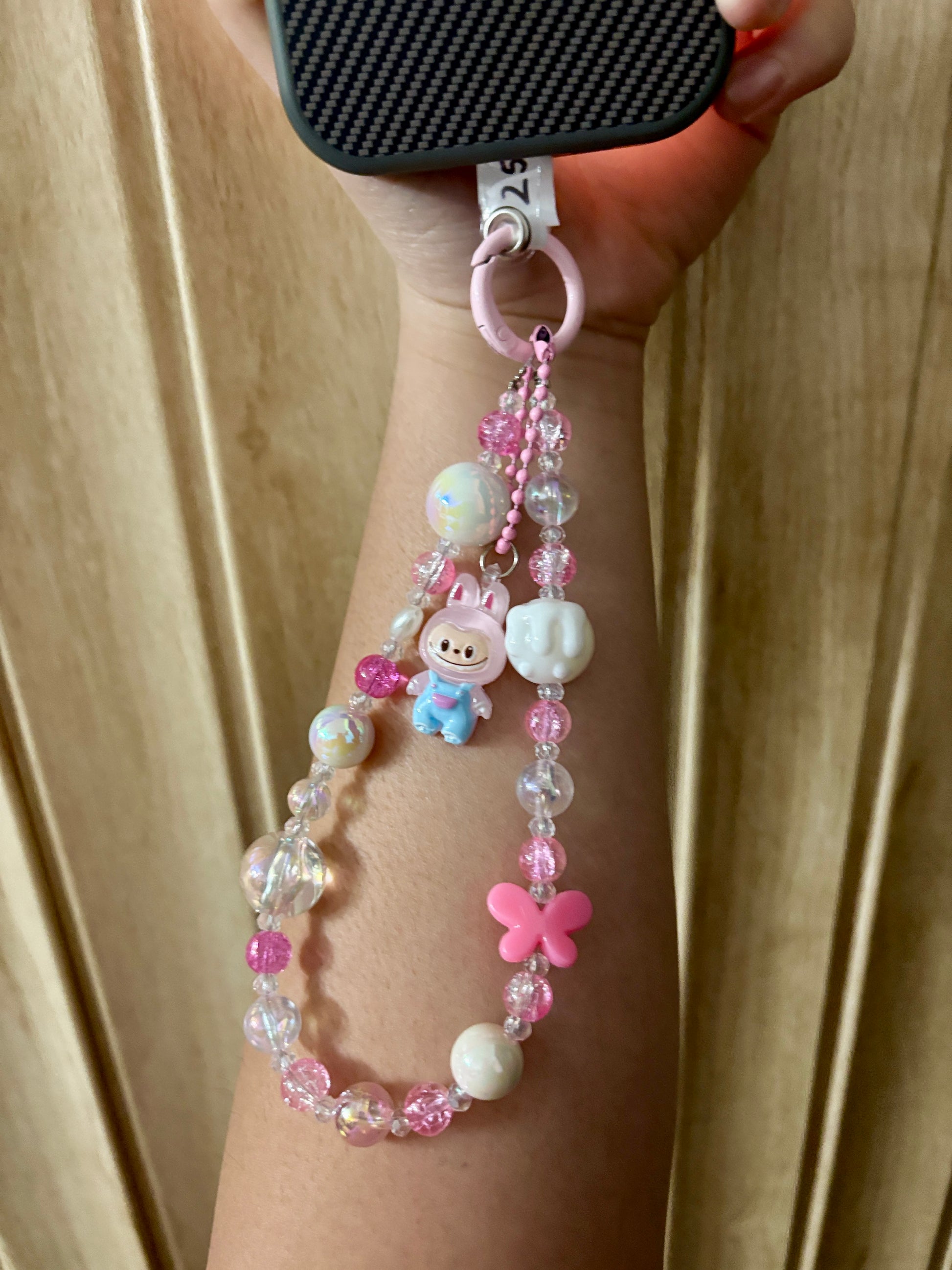 Close-up of a pink Labubu phone charm strap featuring clear and glitter beads, butterfly detail, and the rare Labubu figure — now available in three colors.