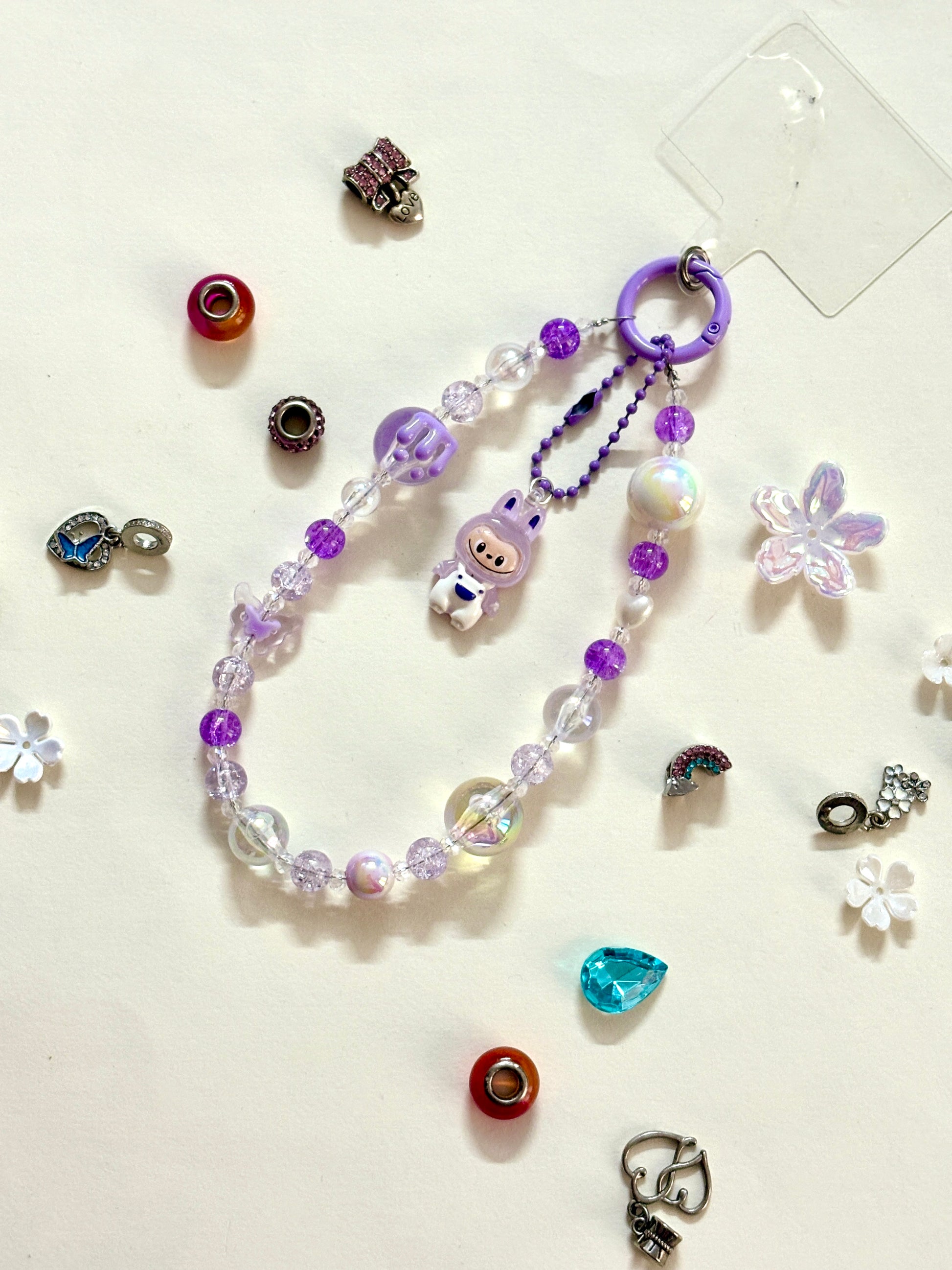 Close-up of a purple Labubu phone charm strap featuring clear and glitter beads, butterfly detail, and the rare Labubu figure — now available in three colors.